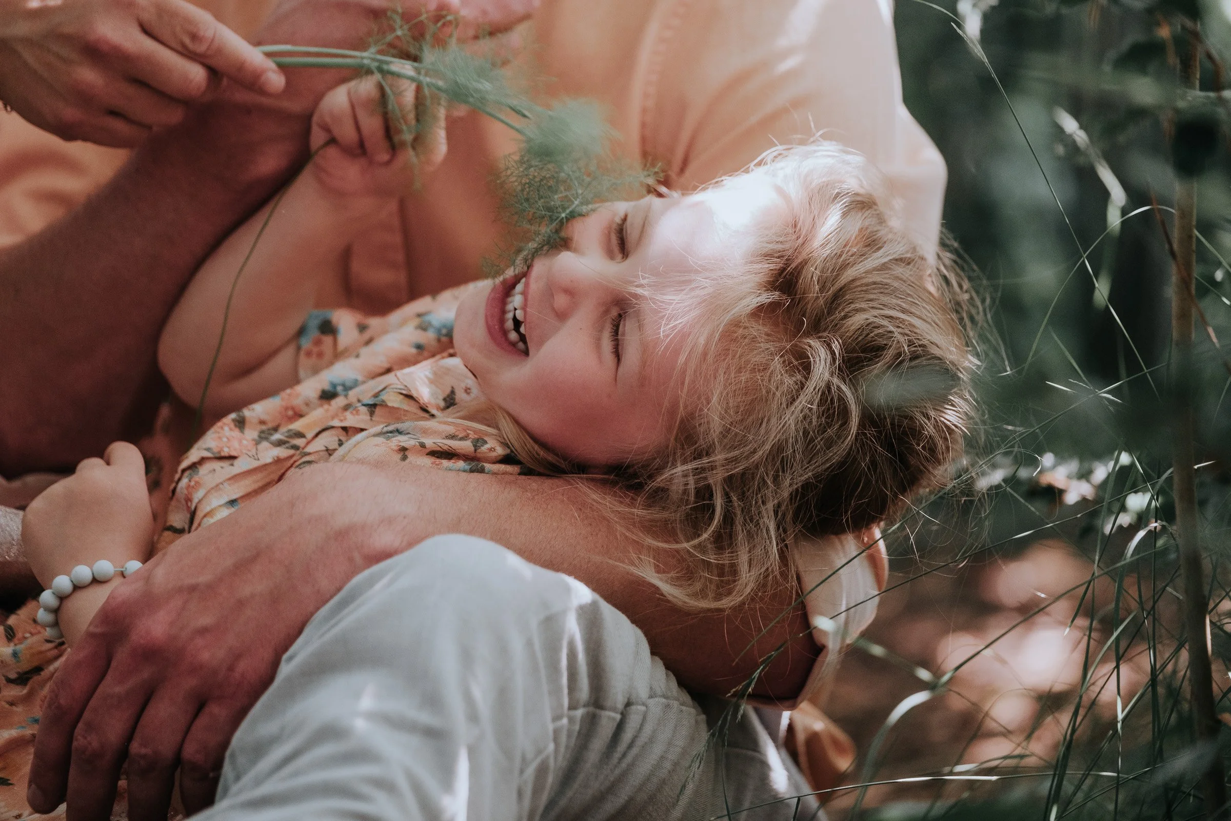 A woman and a child are lying down among plants, smiling and enjoying each other's company.