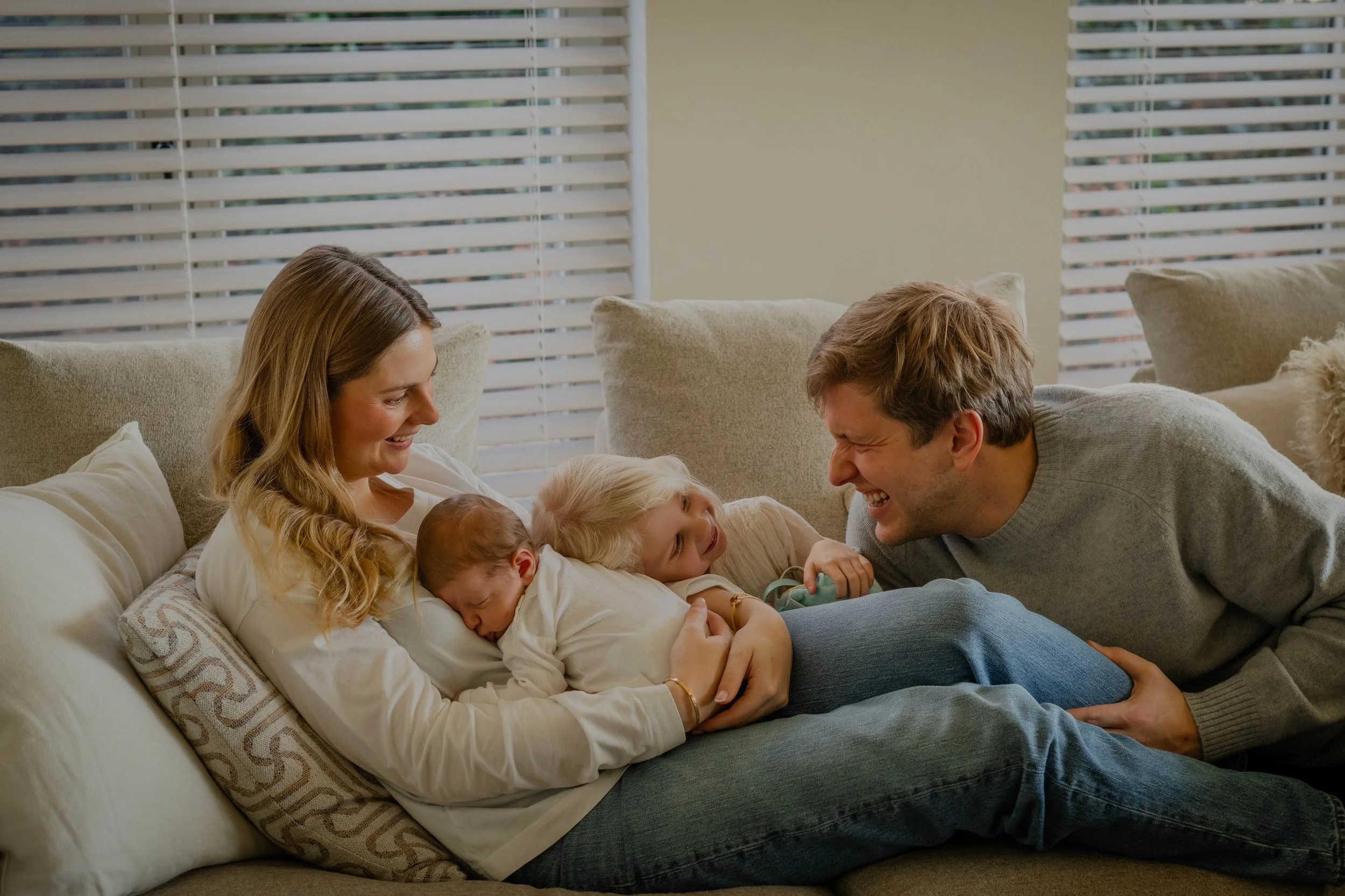 spontane knuffel in de zetel van ouders met newborn en zusje tijdens newborn fotoshoot