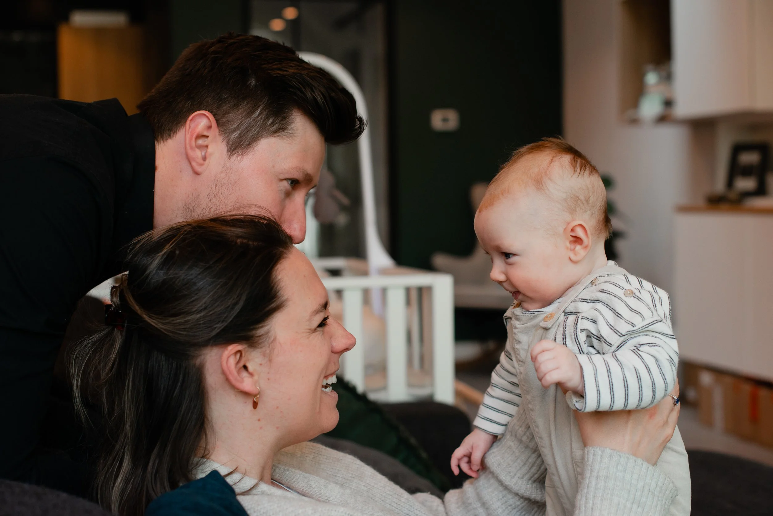 Two women holding a baby boy near their faces in a cozy indoor setting.