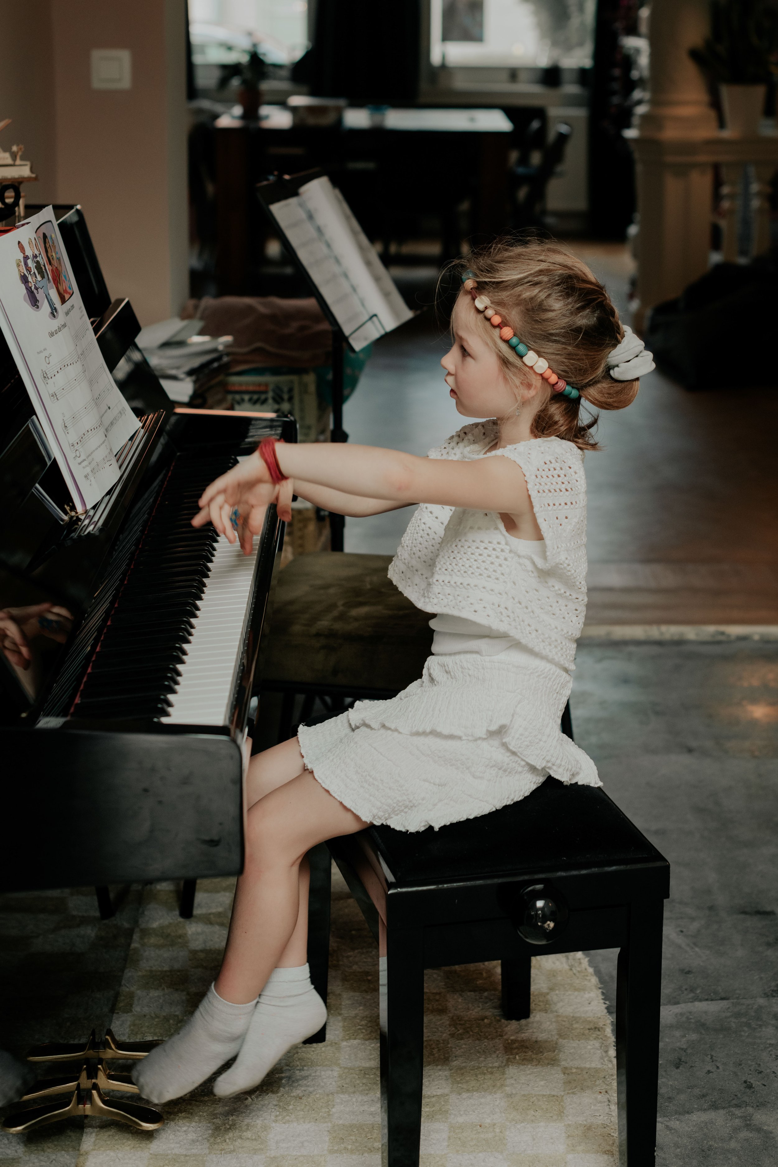 A young girl with a beaded hairband playing the piano in a cozy, well-lit room.