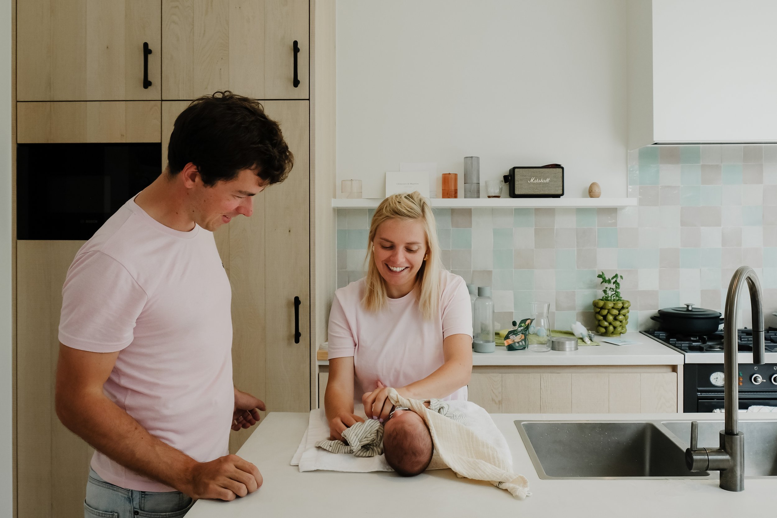 A couple with a newborn baby in a modern kitchen, engaging in a moment of joy and bonding.