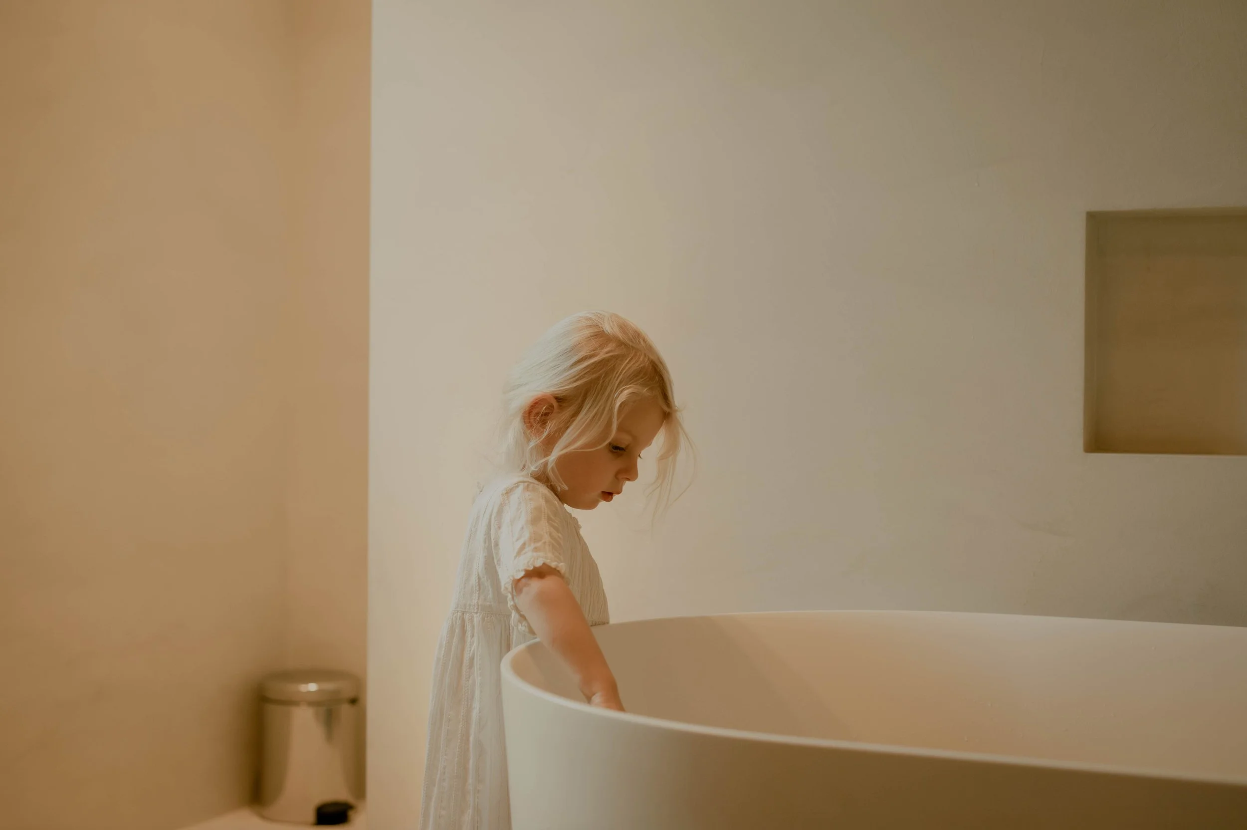 Young girl with blonde hair playing a white grand piano in a minimalist room.