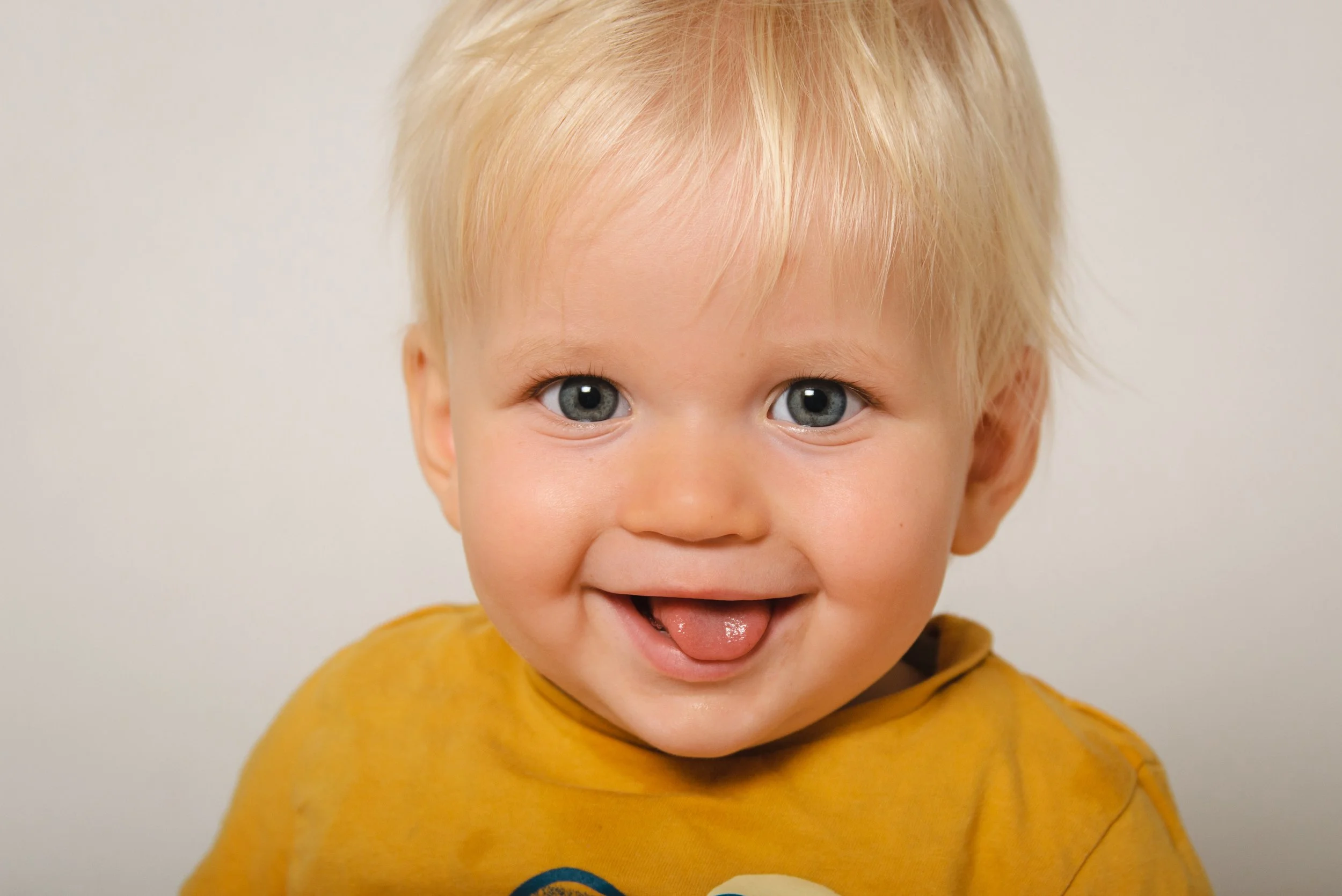 Smiling young boy with blonde hair and blue eyes wearing a mustard yellow shirt.