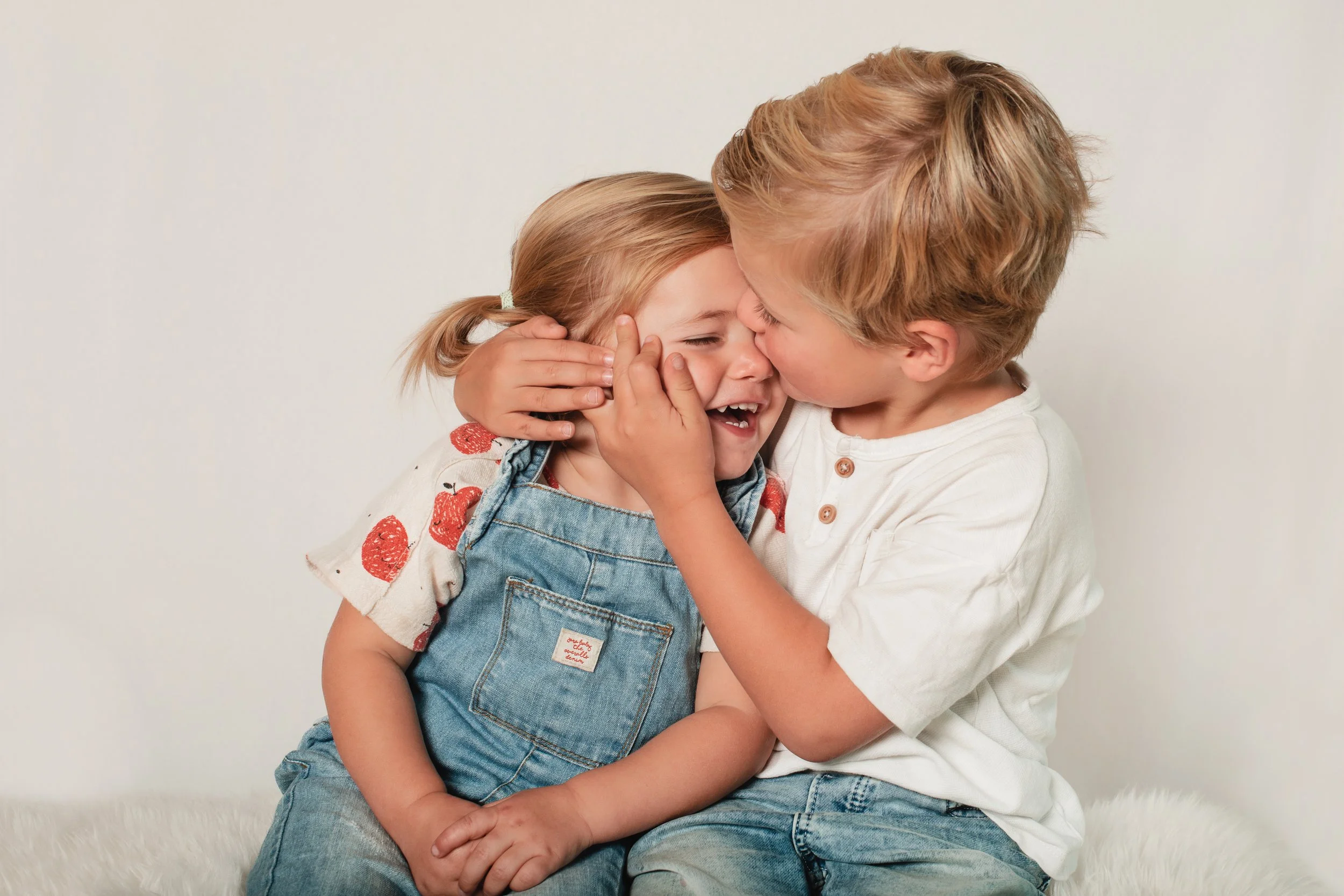 A young boy and a young girl sharing a tender moment, with the boy gently kissing the girl on her forehead and holding her face, both smiling with closed eyes.
