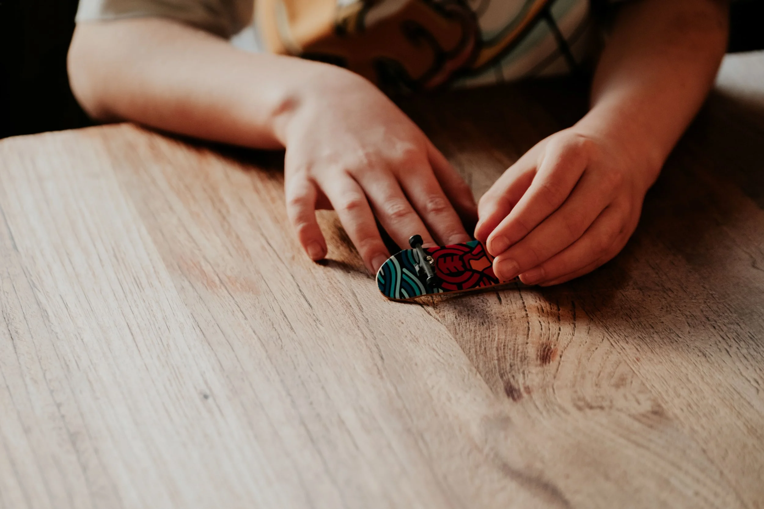 A person's hands holding a colorful patterned harmonica while resting on a wooden surface.