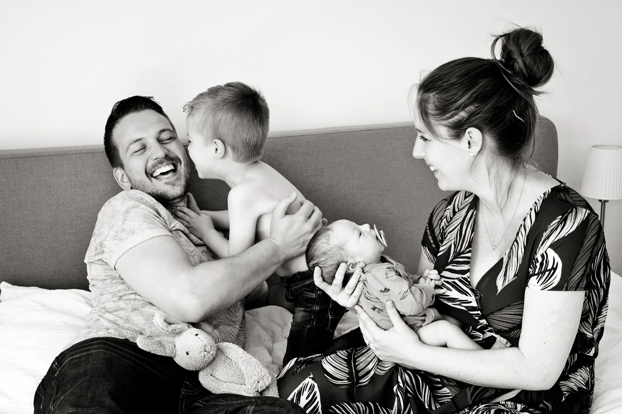 A happy family in a hospital room with a father, mother, and three young children, all smiling and interacting affectionately.