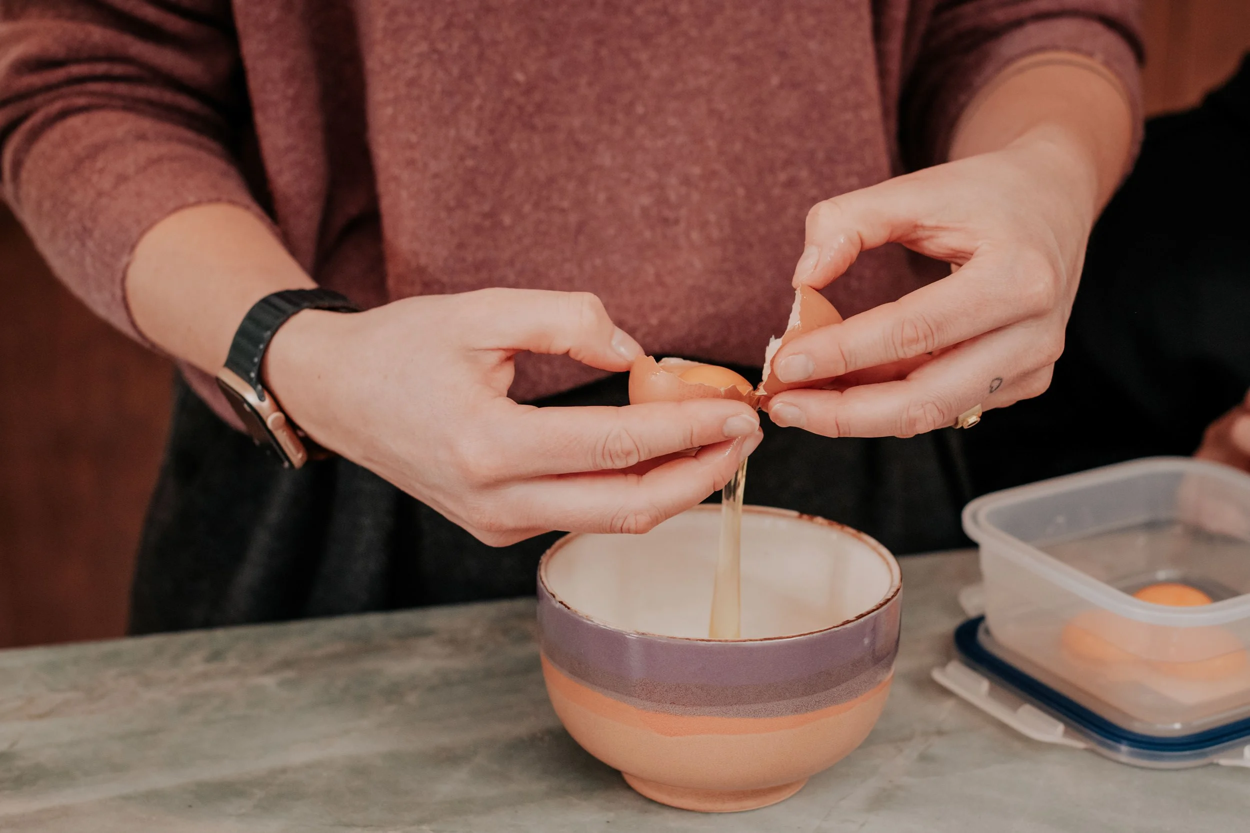 Person cracking an egg into a colorful ceramic bowl.