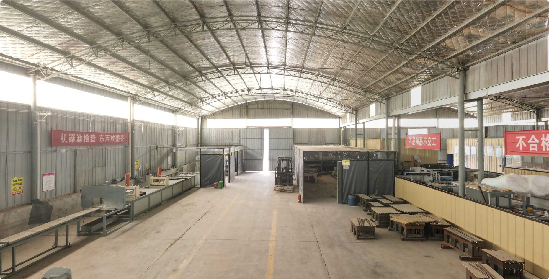 Interior view of a large industrial warehouse or factory with metal walls and ceiling. Various industrial equipment, workstations, and storage areas are visible, with signs in Chinese hanging on the walls.