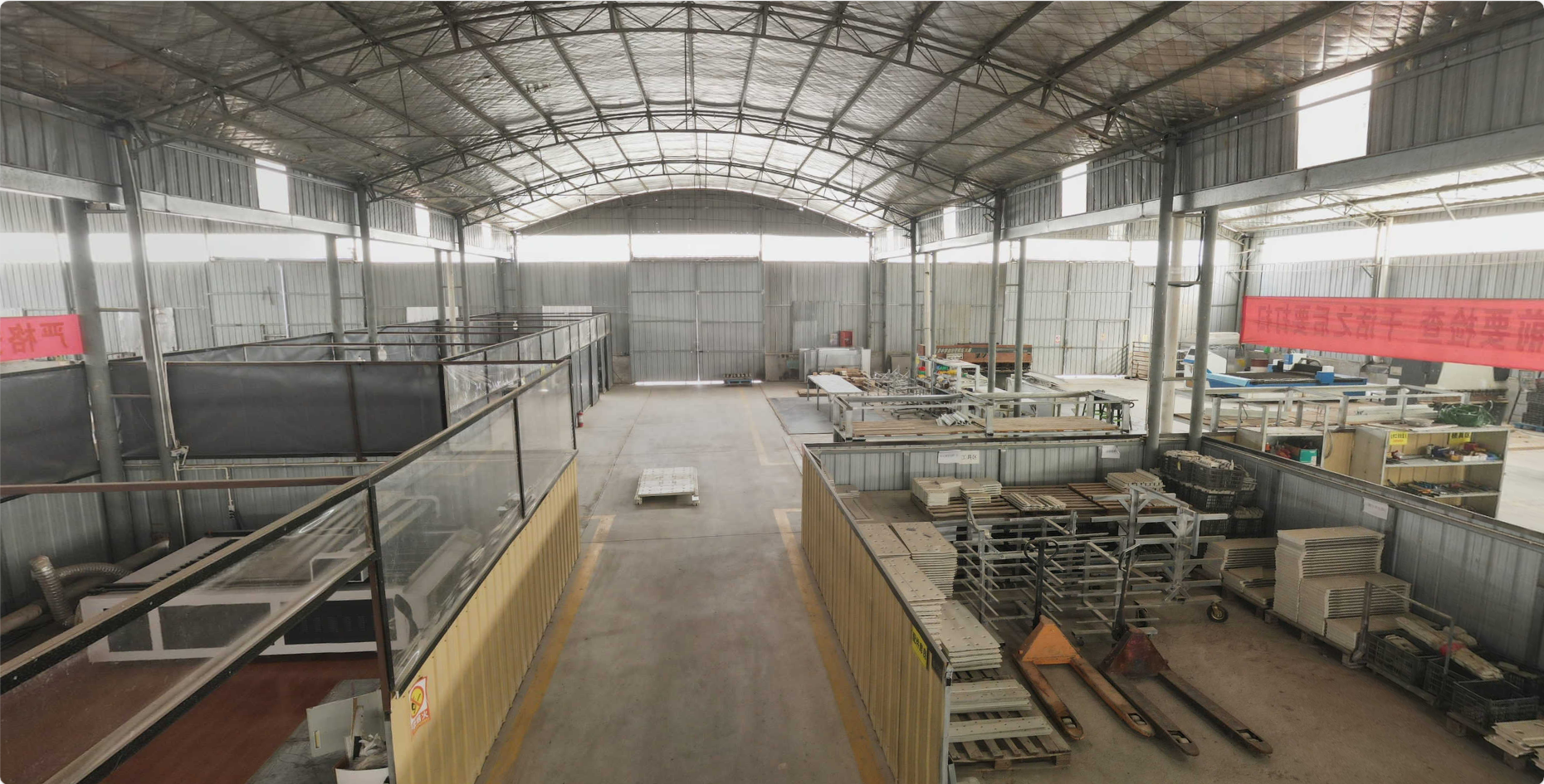 Empty industrial warehouse with metal walls and ceiling, containing storage shelves, pallets, and equipment.