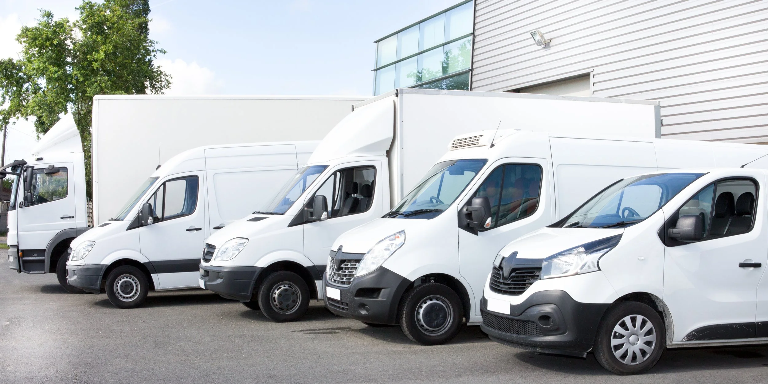 Alignement de plusieurs camionnettes blanches garées près d'un bâtiment industriel.