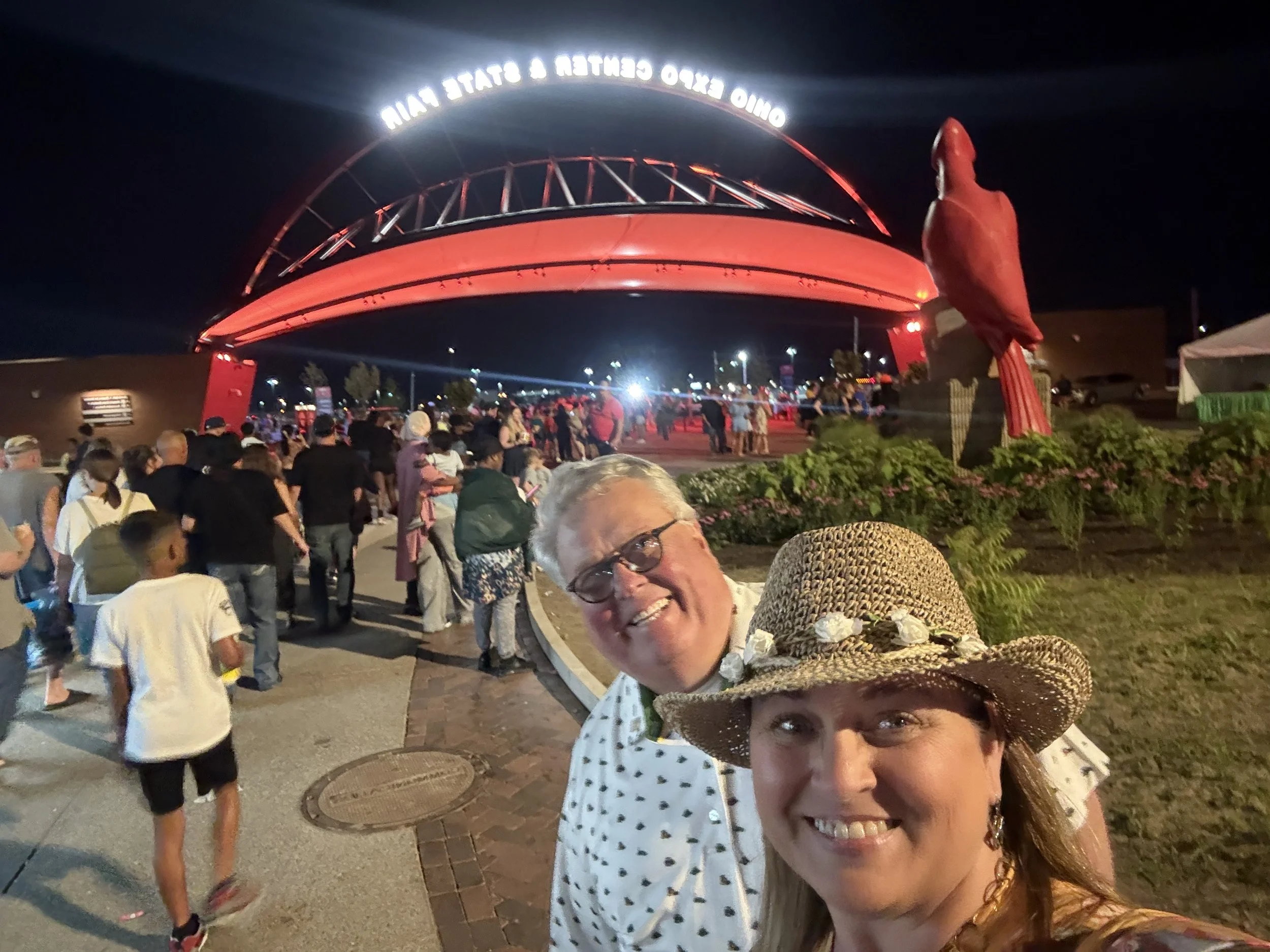 Crowd gathered outside the Expo Center & State Fair at night, with a large red-lit arch and people wearing hats and casual clothing.