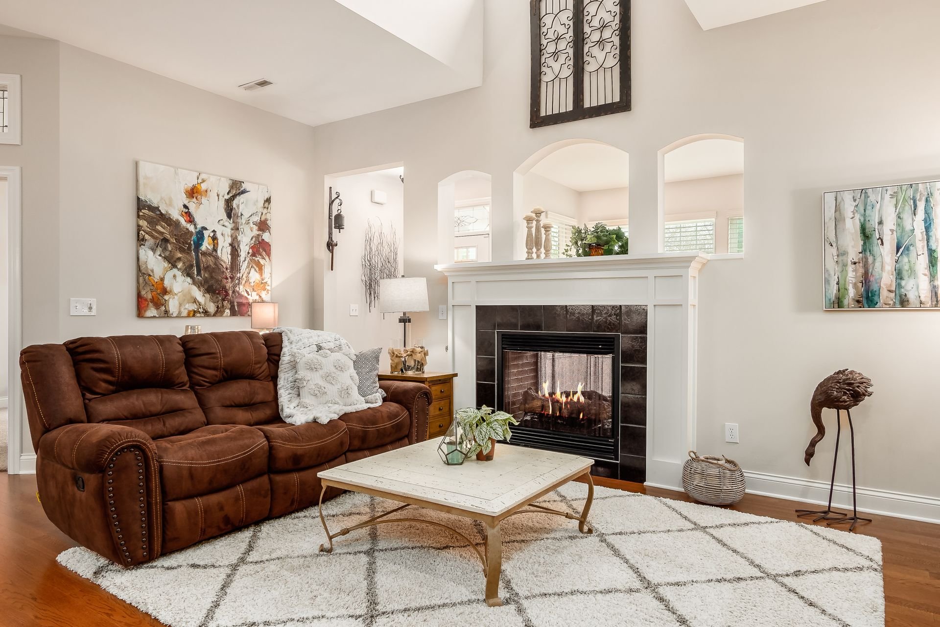Living room with a brown sofa, a white coffee table, a fireplace, and colorful abstract paintings on the wall.