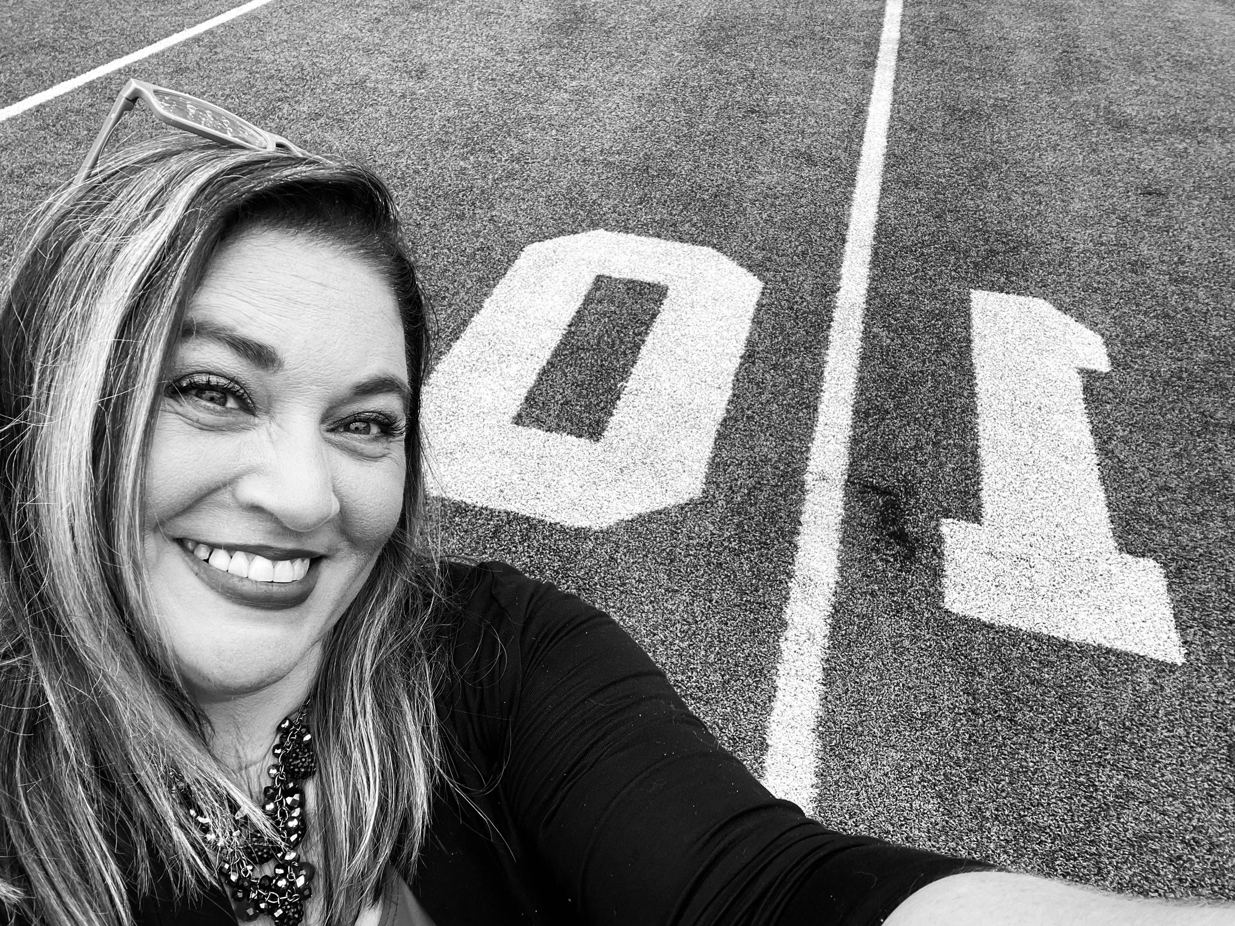 A woman smiling taking a selfie on a running track with white lane markings, including a curved arrow painted on the track.