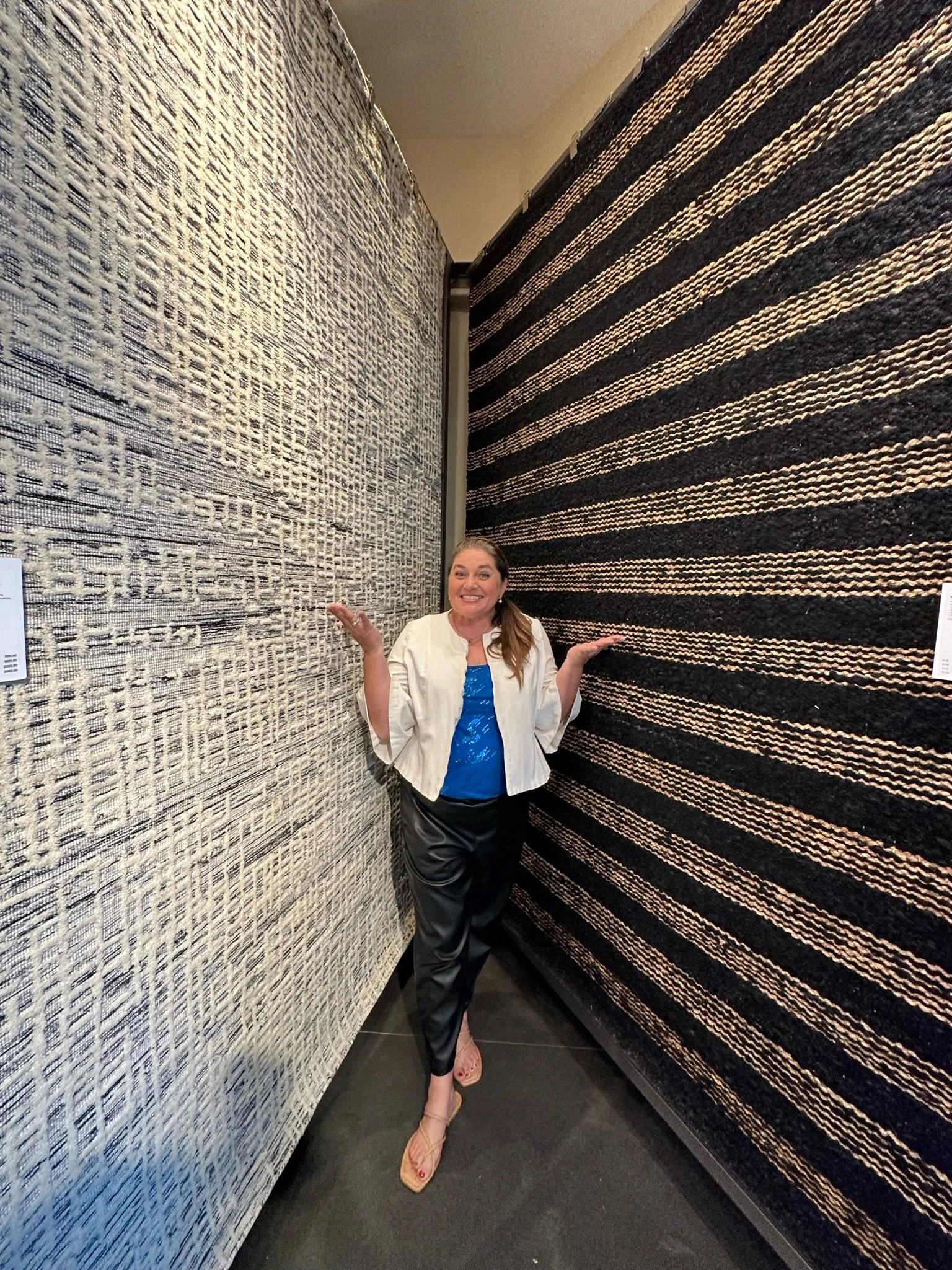 A woman standing between two large, textured, striped wall hangings in an art gallery, smiling and posing with her hands raised.