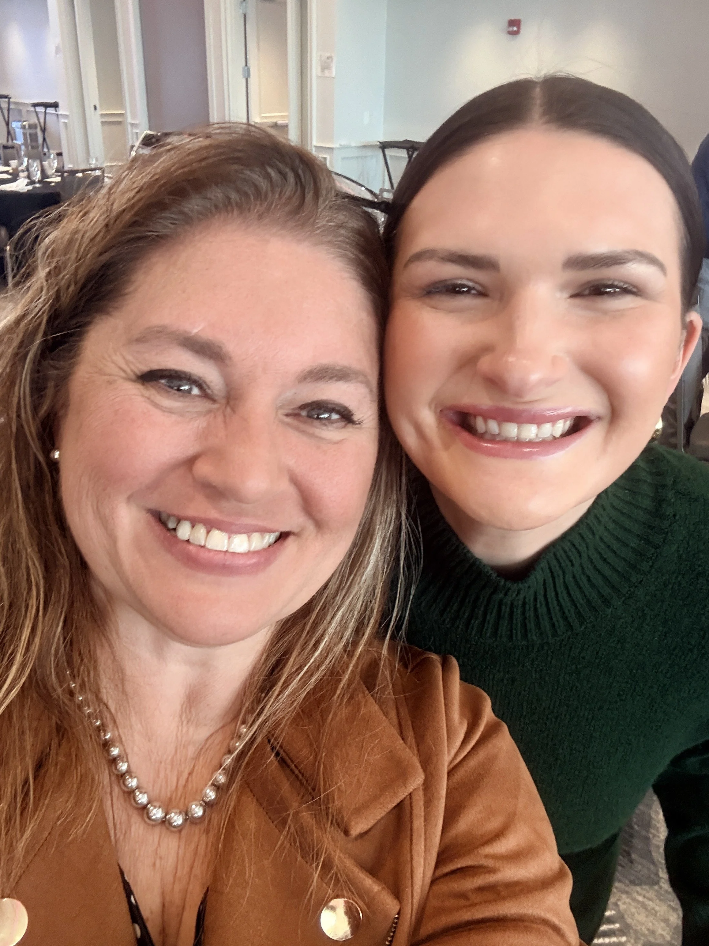 Two smiling women taking a close-up selfie at a social gathering.