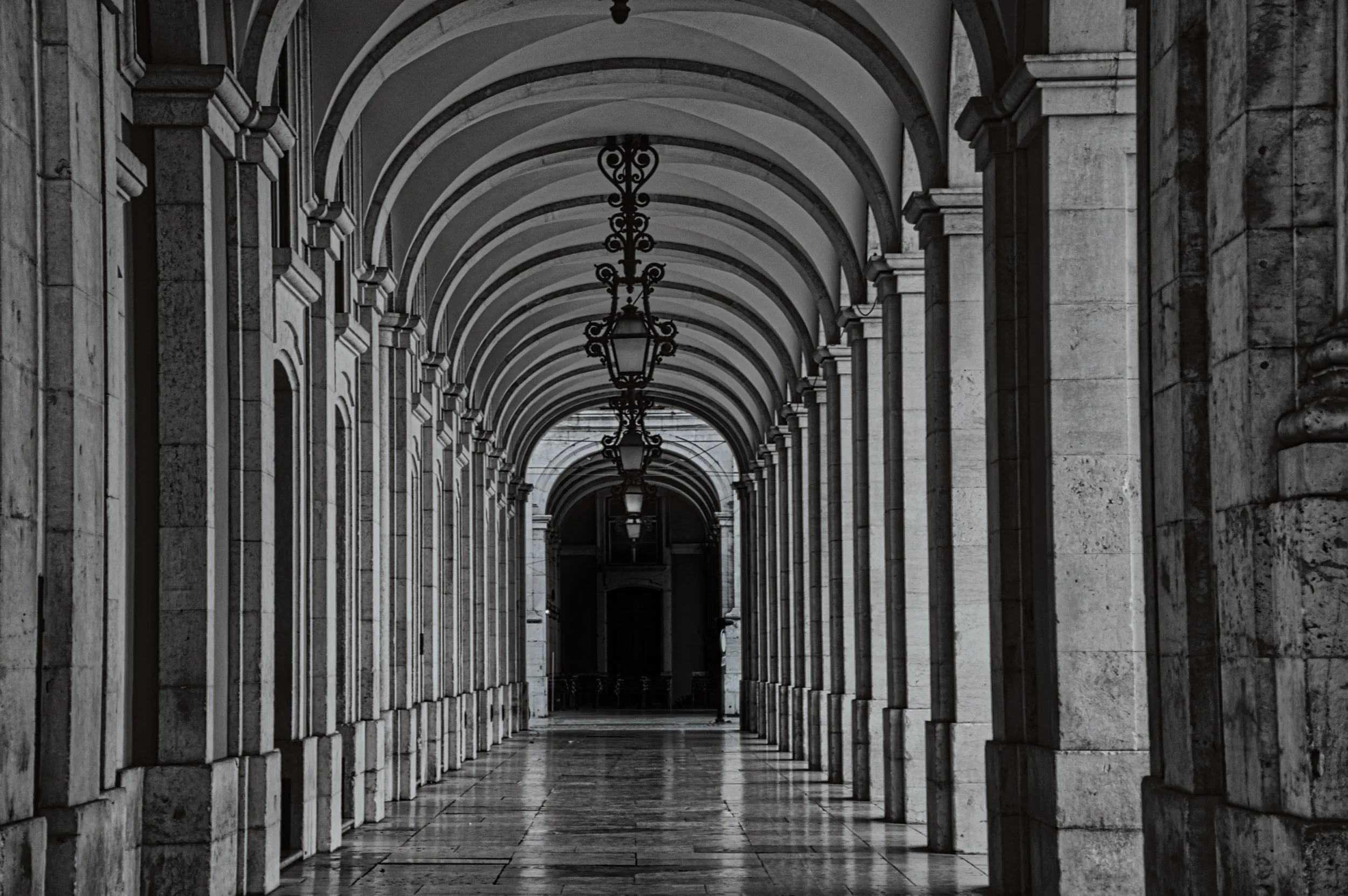 Corredor com arcos de pedra e luminárias penduradas de ferro