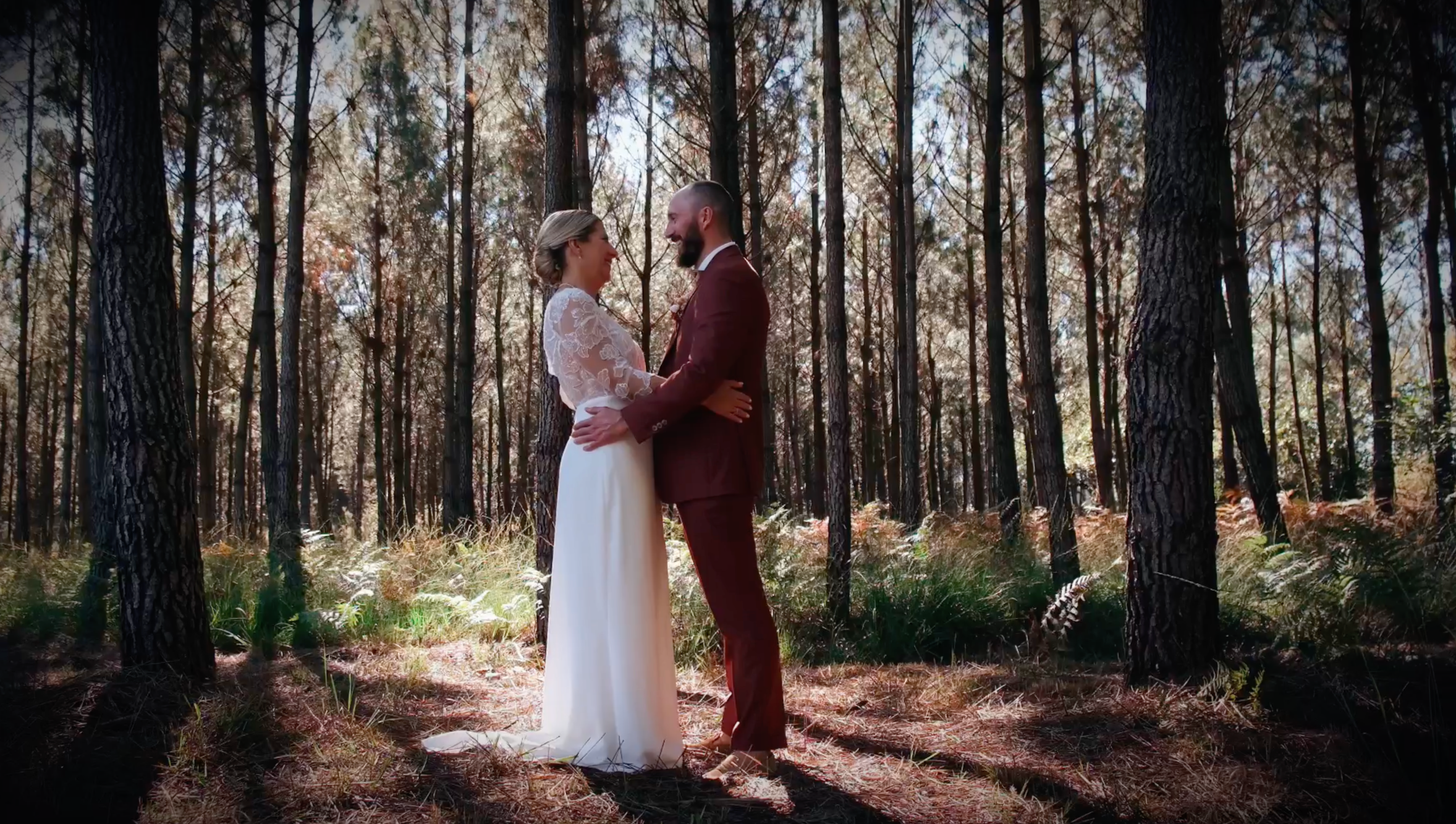 Un couple lors d'un mariage dans une forêt, ils se tiennent face à face, souriant et se regardant tendrement, entourés d'arbres et de lumière naturelle.