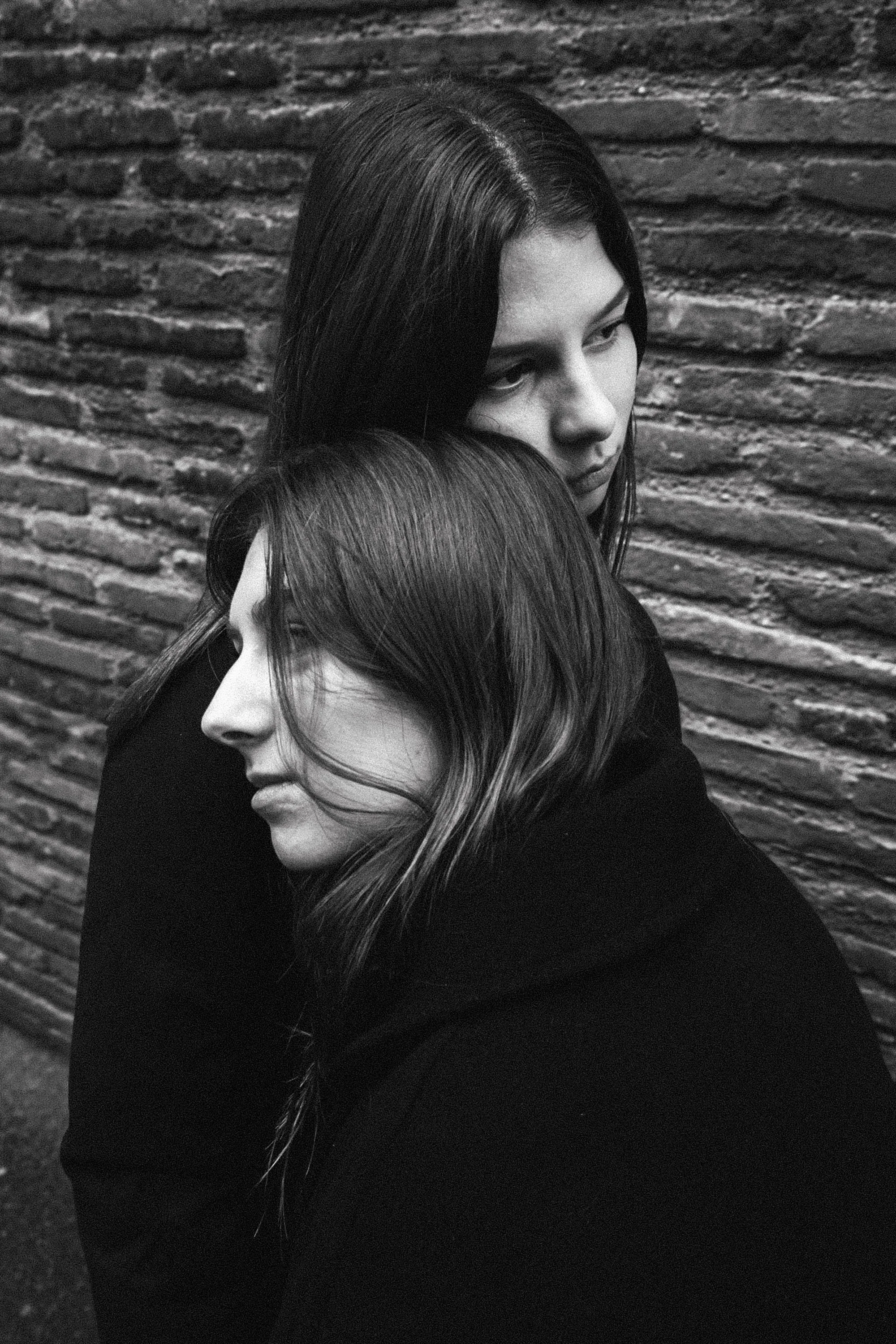 Deux femmes aux cheveux longs et foncés en portrait noir et blanc, se tenant près d'un mur en briques.