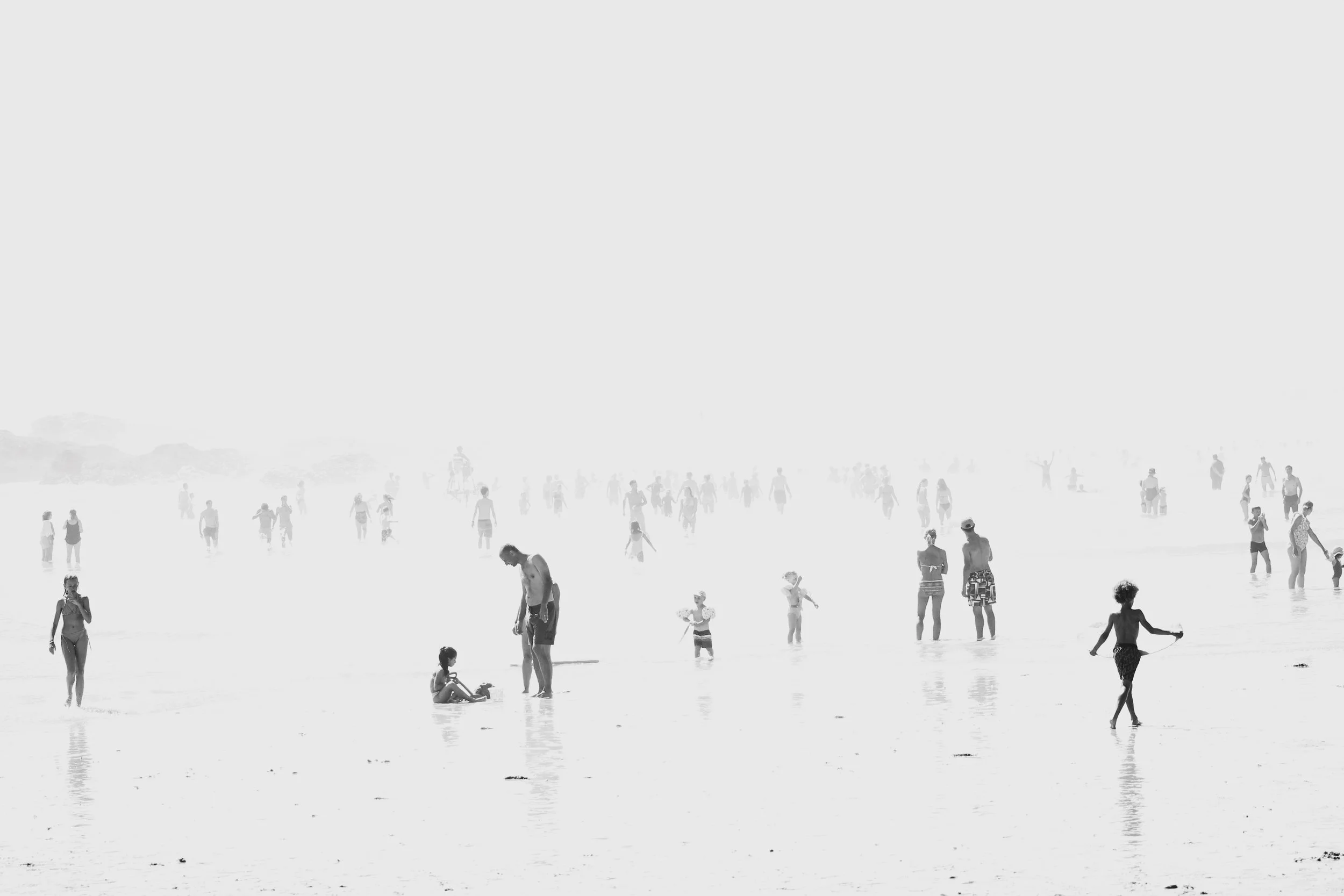De nombreuses personnes profitent d'une journée à la plage, se baignant, jouant et se détendant dans l'eau et sur le sable.