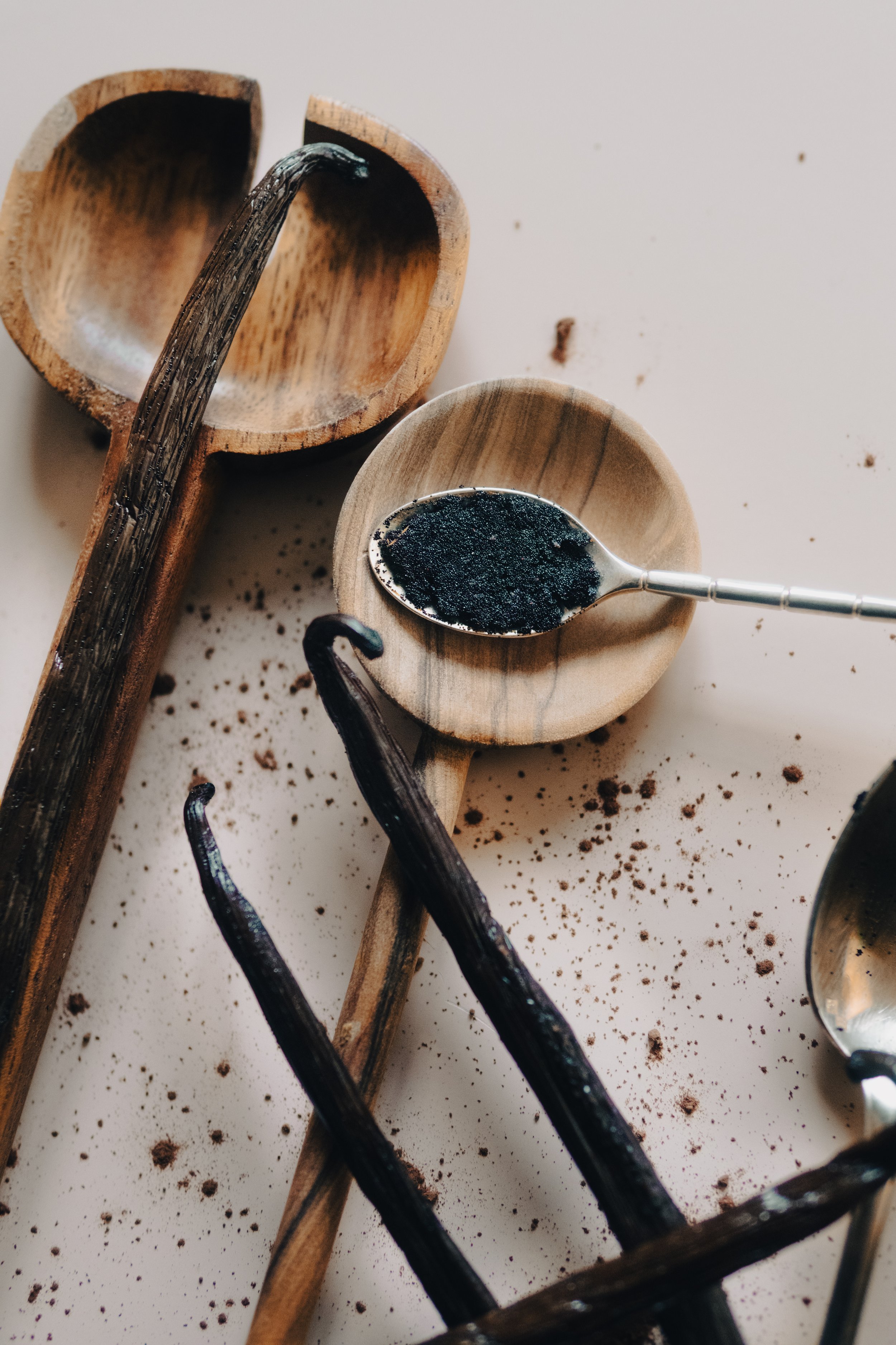 Cuillères en bois avec de la poudre ou de la pâte noire, brouhaha de poudre éparpillée sur une surface blanche.