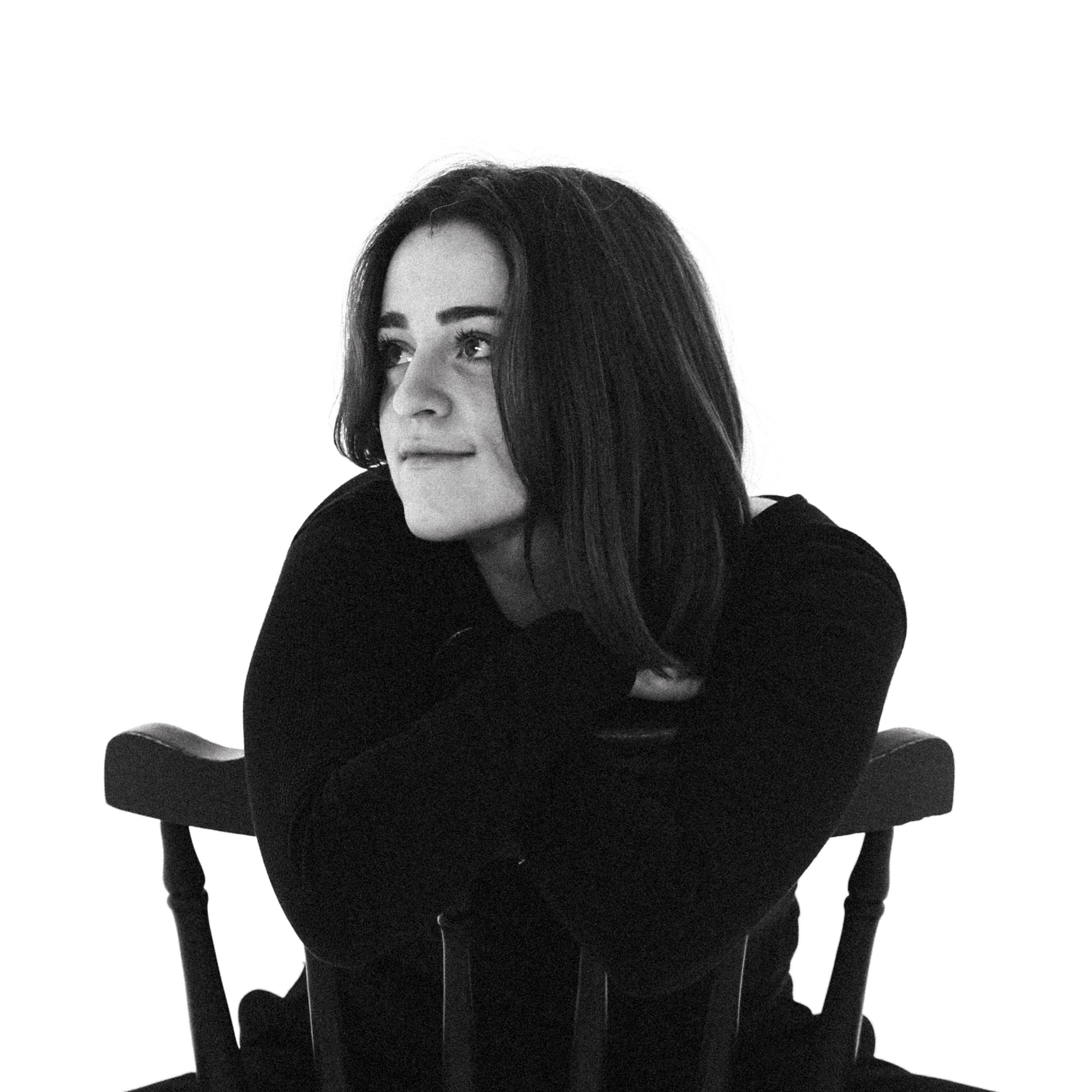 Portrait noir et blanc d'une femme avec de longs cheveux foncés, portant un vêtement sombre, regardant vers la gauche.