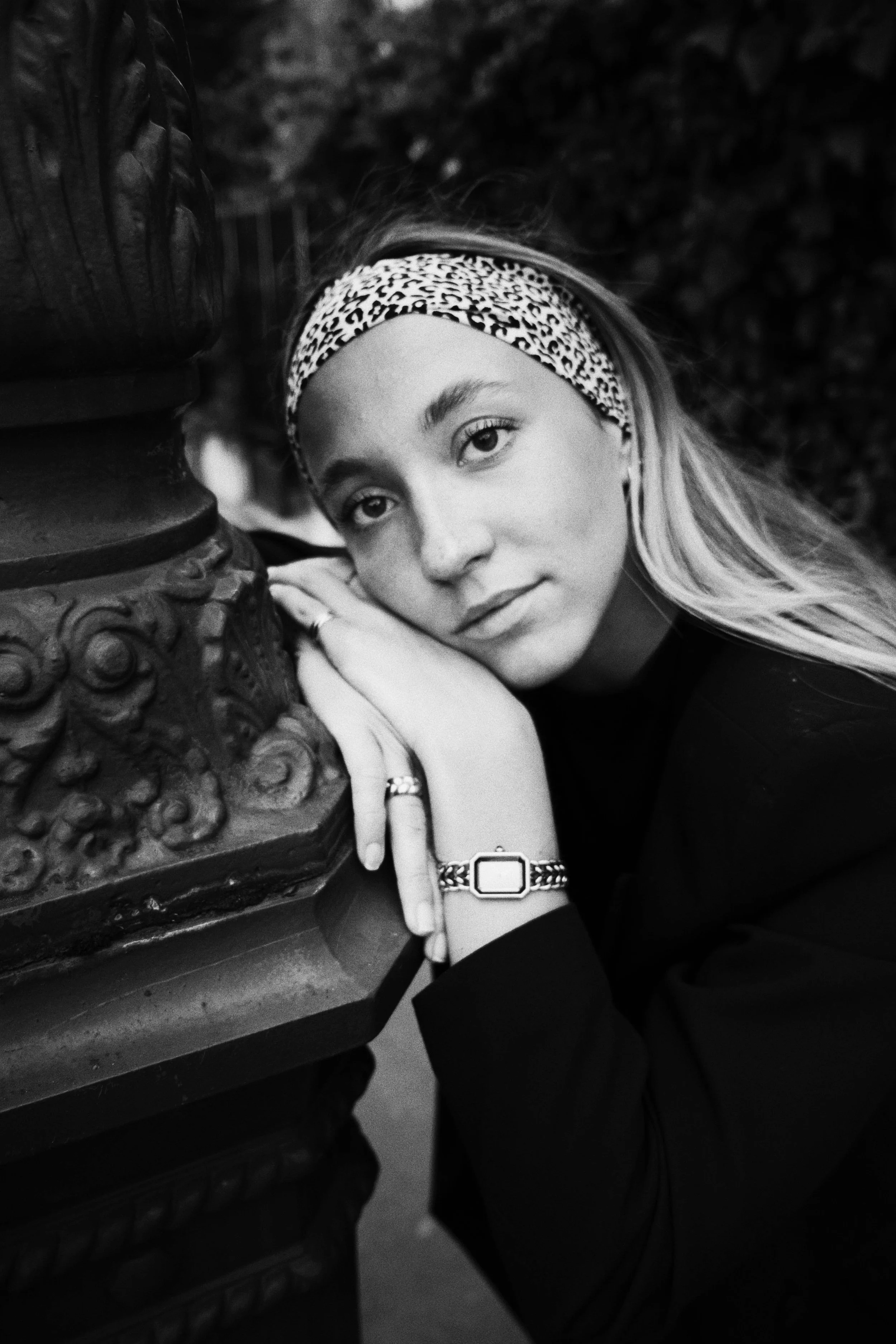 Une jeune femme avec une bandeau animal print sur la tête, tenant sa main près d'un objet en bois sculpté et portant une montre et plusieurs bagues, regardant vers l'objectif.