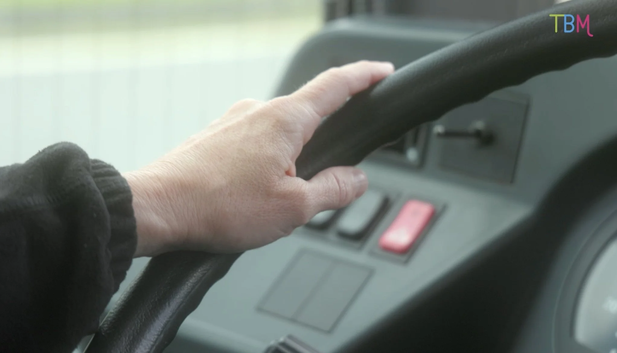 Une main qui tient le volant d'une voiture alors que l'on voit le tableau de bord de la voiture.