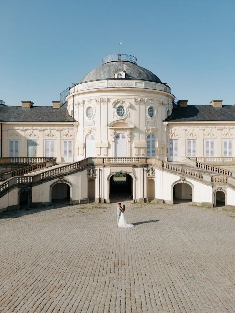 After-Wedding-Shooting Schloss Solitude Stuttgart, Brautpaar  in der Mitte des Schlossvorplatzes mit Blick auf das Hauptgebäude.