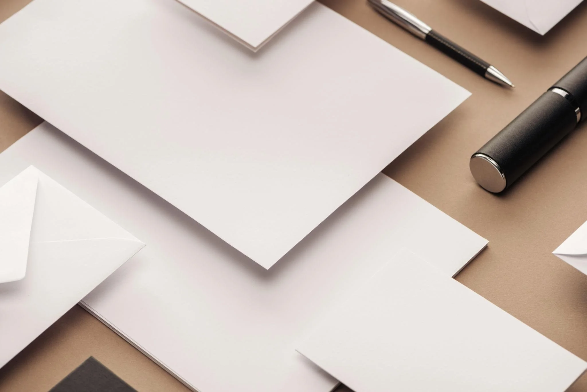 various sheets of white paper, a black pen, and a black flashlight on a brown background
