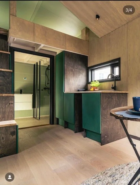 Lite kjøkkenområde med grønn og mørkebrun skap, vindu med utsikt, og et spisebord med en blå kopp på. Foto: Thomas Larsen 