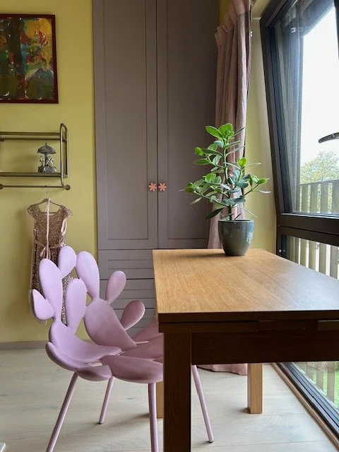 Et rom med et bord, en plante i en pot, en vinduskarm, en garderobe, en barneklær og et maleri på veggen.