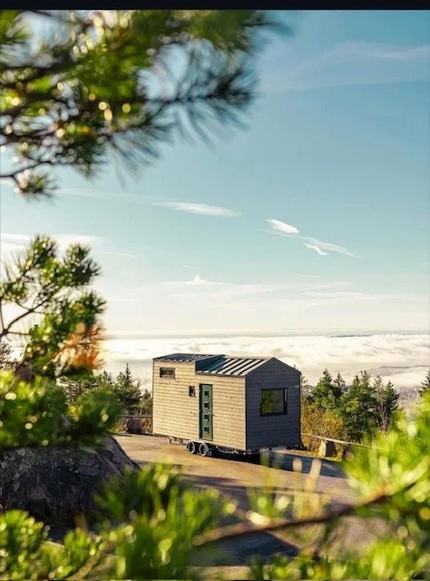 En liten flytende hytte på en fjelltopp med utsikt over landskap og skydekket hav, omgitt av trær. Foto: Thomas Larsen 