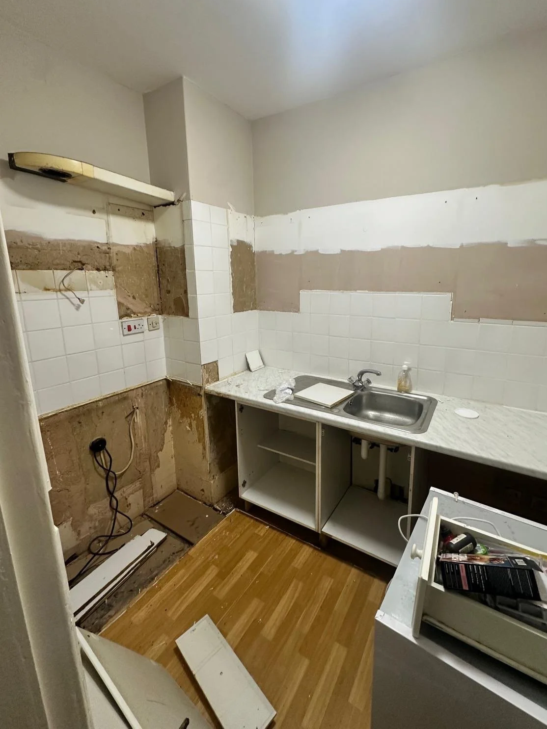 Kitchen with unfinished walls and cabinets, a small sink, and scattered construction materials.