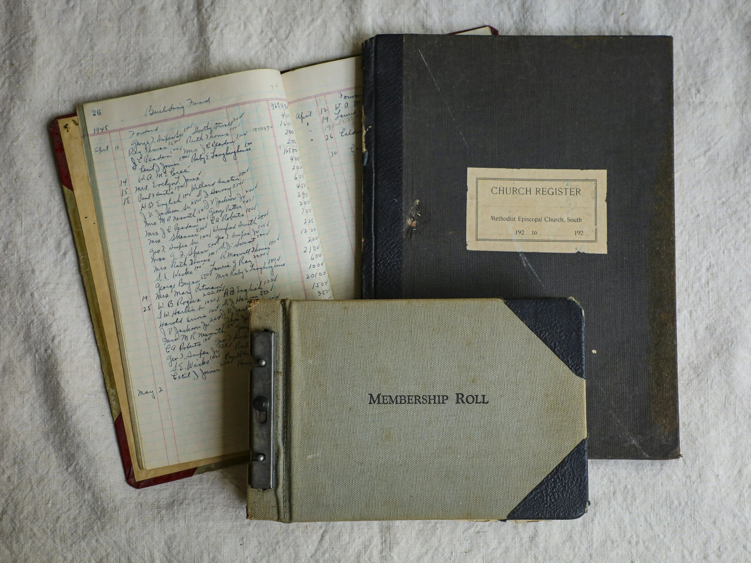 Close-up of vintage church membership and church register book on a textured surface, with handwritten entries and a black hardcover membership roll book.