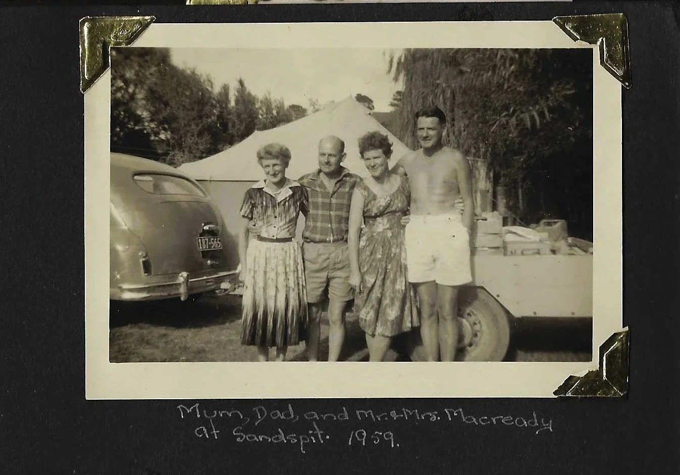 Captured on a classic black album page, this showcases two vintage mid-century photographs preserved with decorative brass corners. The handwritten caption in white ink dates the top camping scene to 1959 at Sandspit, featuring the user’s parents and