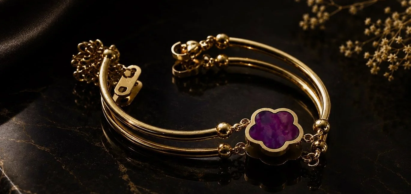 Gold bracelet with purple floral-shaped pendant on a black surface.