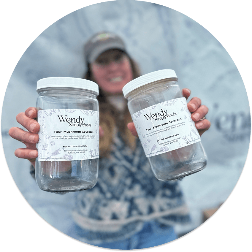 Person holding two jars labeled 'Wendy Simply Cooks' with mushroom couscous, smiling in the background.