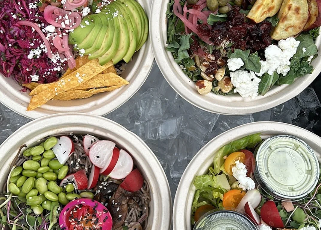 Four bowls of fresh salads with various vegetables and toppings, placed on a bed of ice.