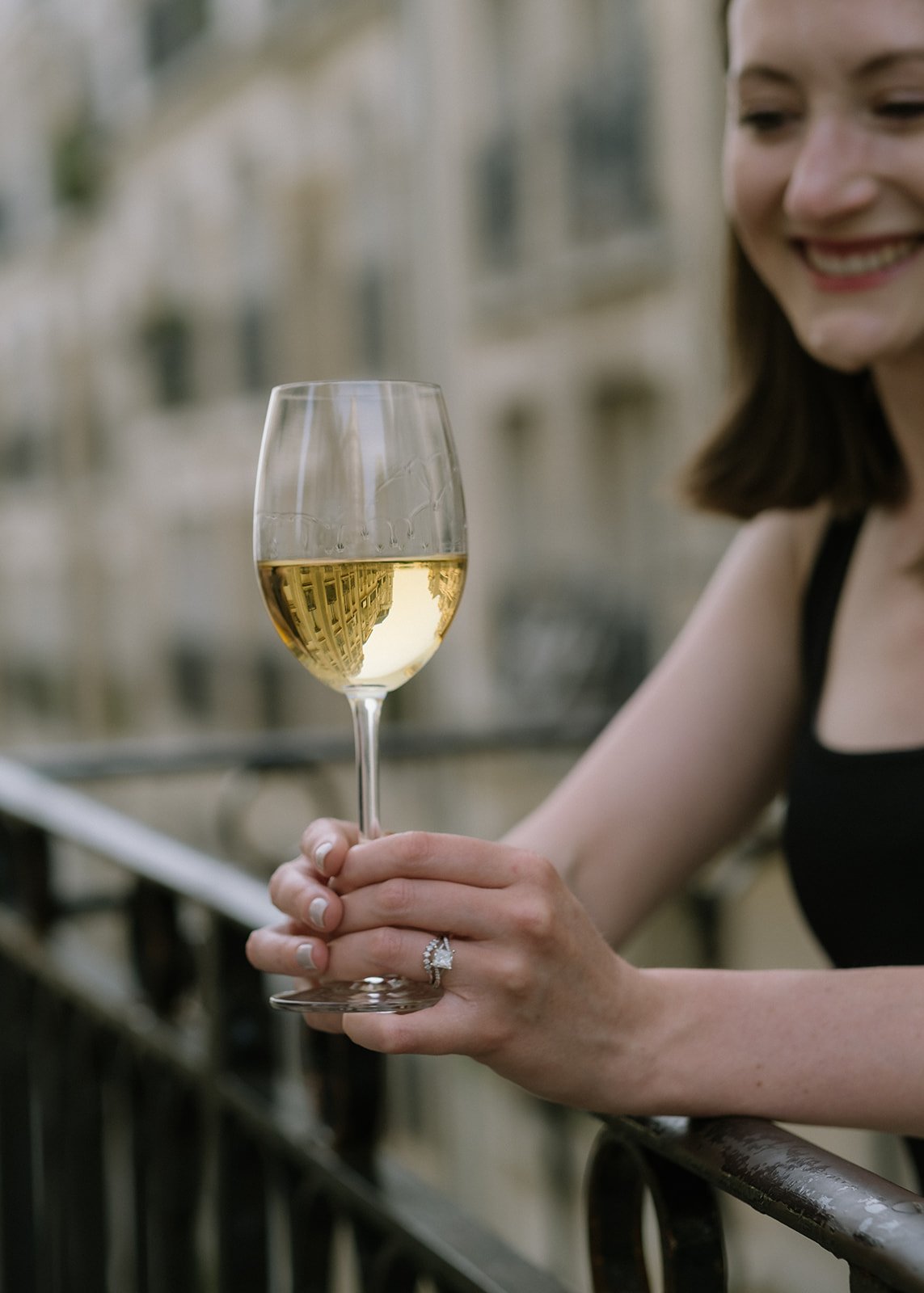 A woman holds a glass of white wine outside.