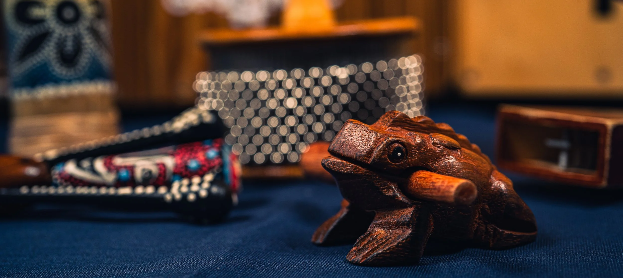 A carved wooden frog figurine with intricate details, surrounded by various decorative items including patterned objects and blurred background elements.