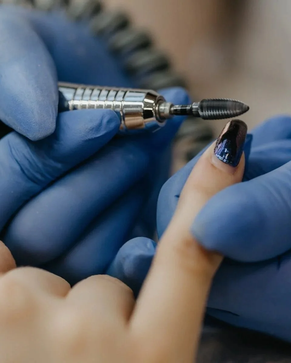 Une personne reçoit un soin de manucure avec un outil électrique pour la pose de vernis ou le traitement des ongles, tenant la main d'une autre personne