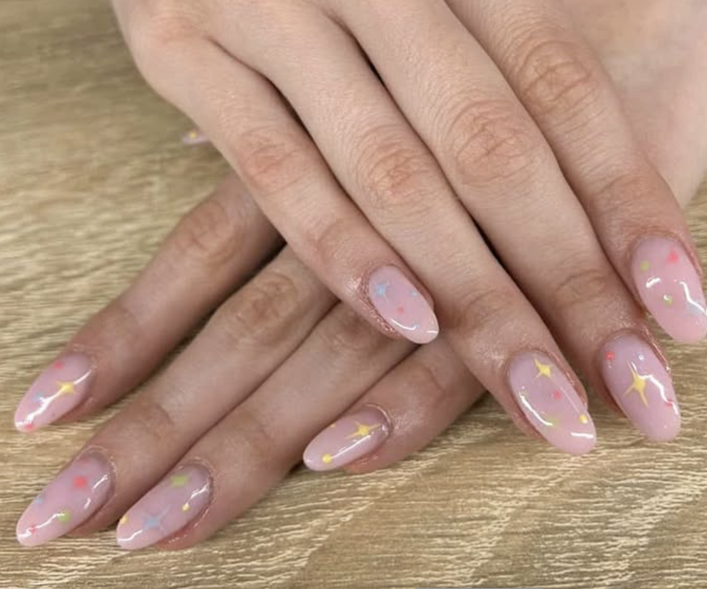 Les mains avec des ongles vernis à ongles pastel rose clair, décorés de petites étoiles et points colorés.