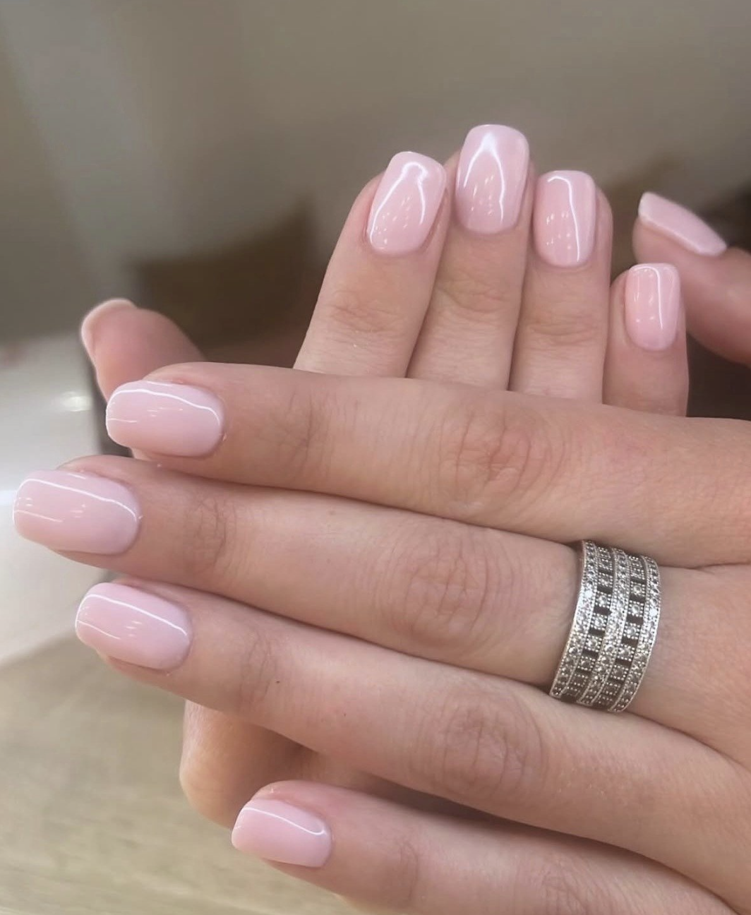 Mains avec des ongles pâles vernis, portant une bague en diamants et anneaux en argent.