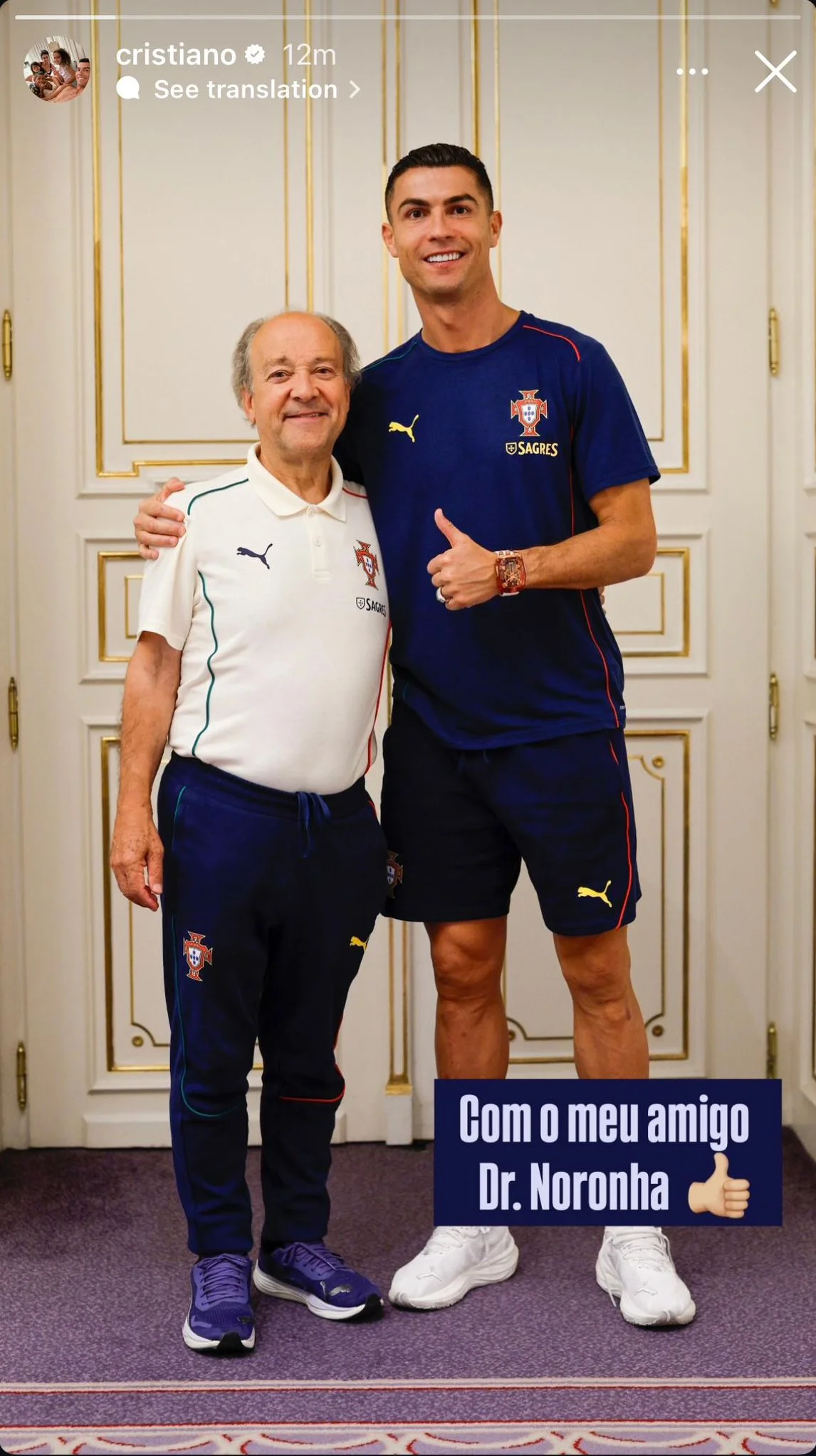 Cristiano Ronaldo ao lado de um homem mais velho, ambos vestindo roupas esportivas da seleção de Portugal, posando juntos em um ambiente interno com fundo de portas brancas e detalhes dourados. Cristiano Ronaldo está vestindo uma camiseta azul com o 
