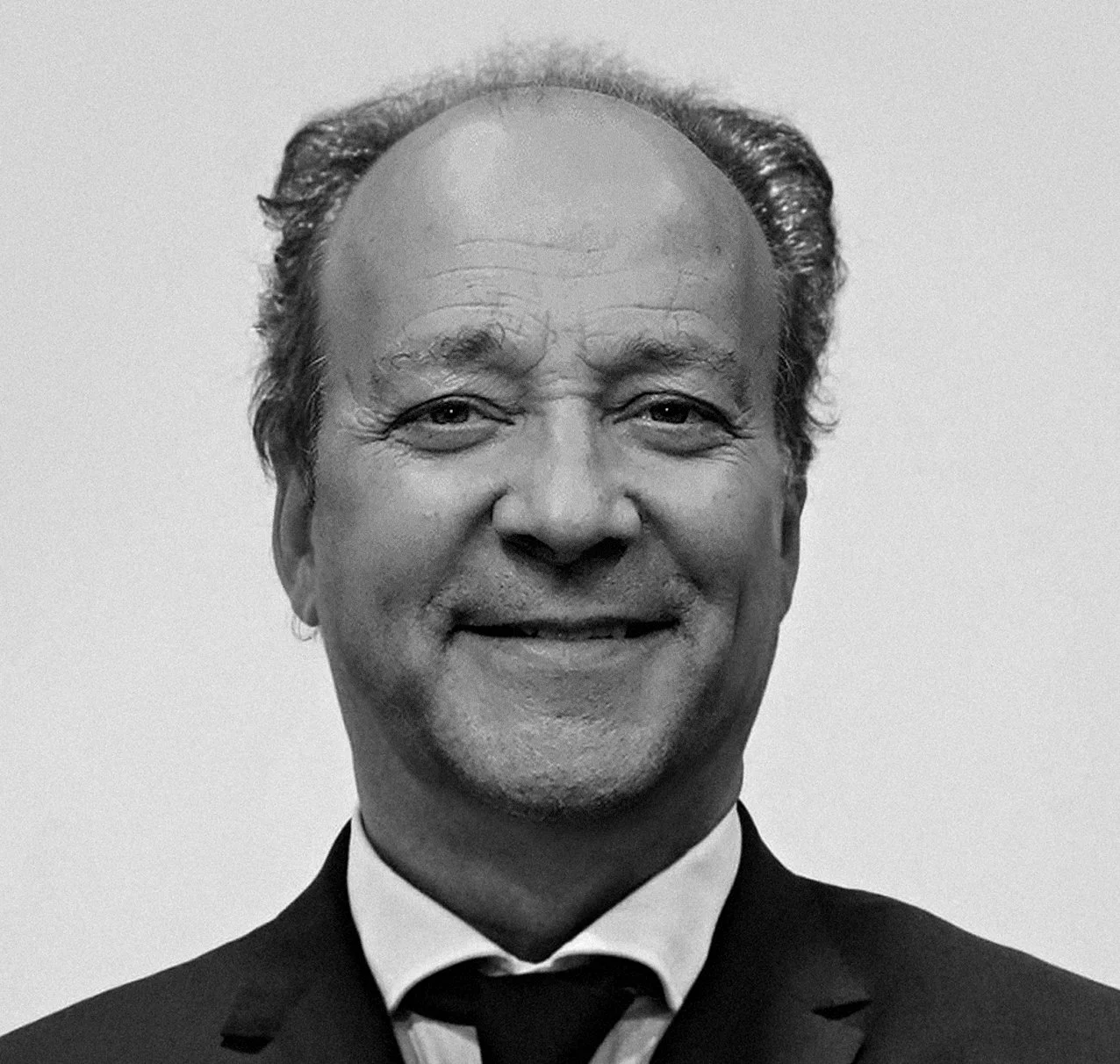 Retrato de um homem sorridente, usando terno e gravata, em preto e branco.