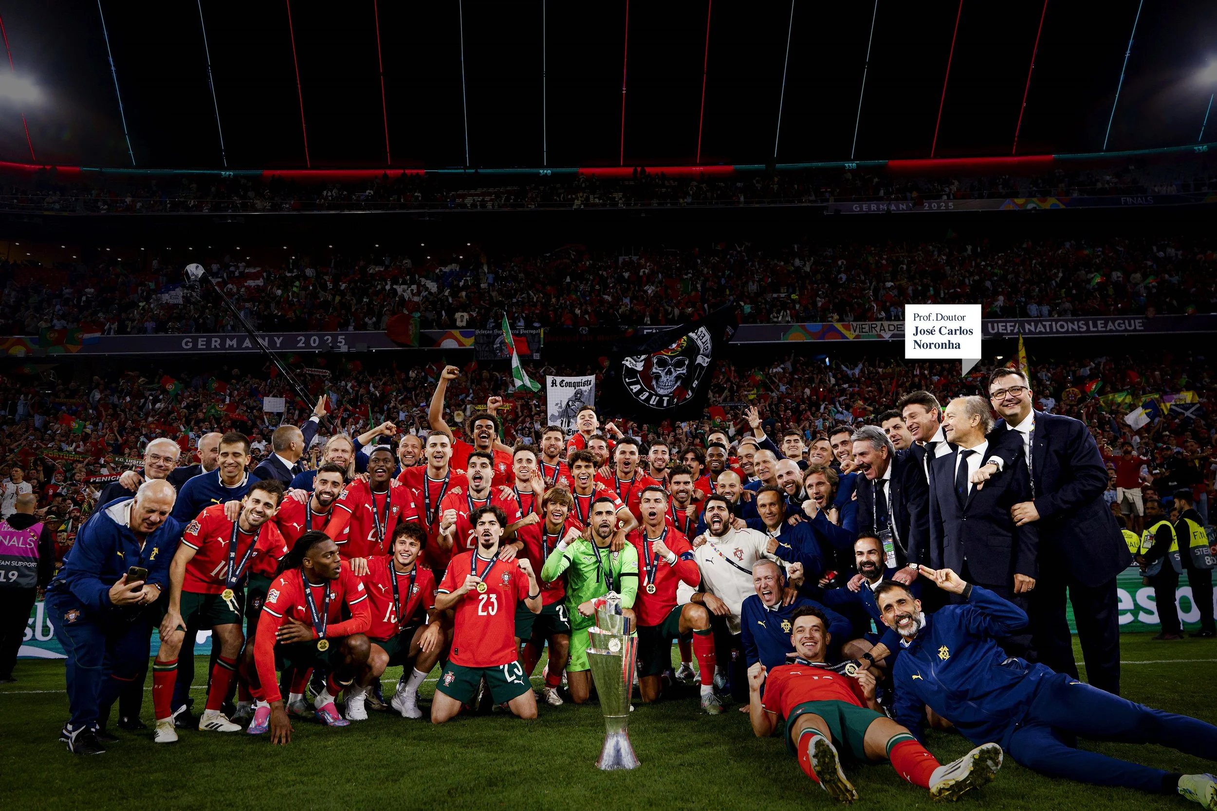Time de futebol celebrando com troféu em um estádio lotado após uma vitória, com jogadores e técnicos sorrindo e levantando os braços, bandeiras e cartazes ao fundo.