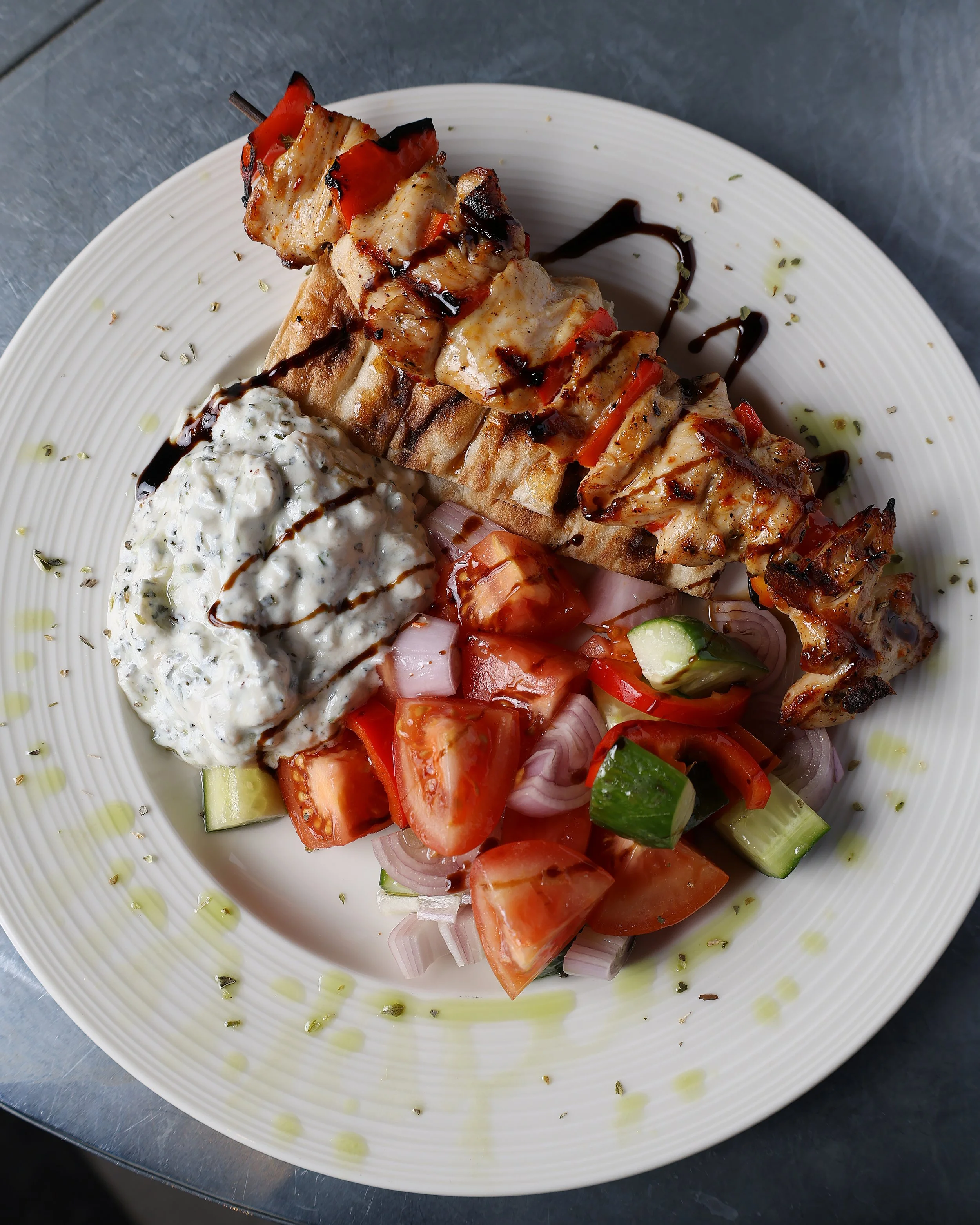 Grilled chicken skewers with red and green peppers on a white plate, garnished with herbs and served with a dollop of herb-infused creamy sauce, drizzled with balsamic glaze.