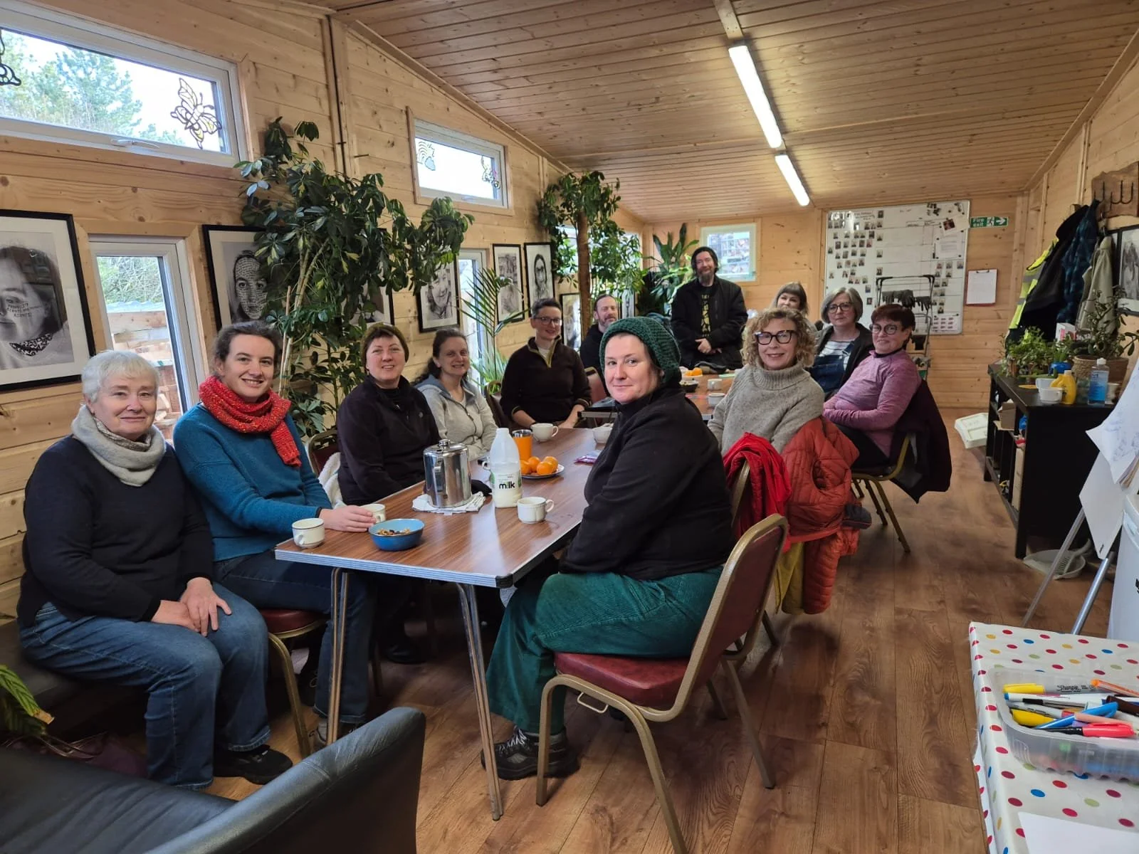 A number of community growers sitting at tables of tea and food in a wooden community building