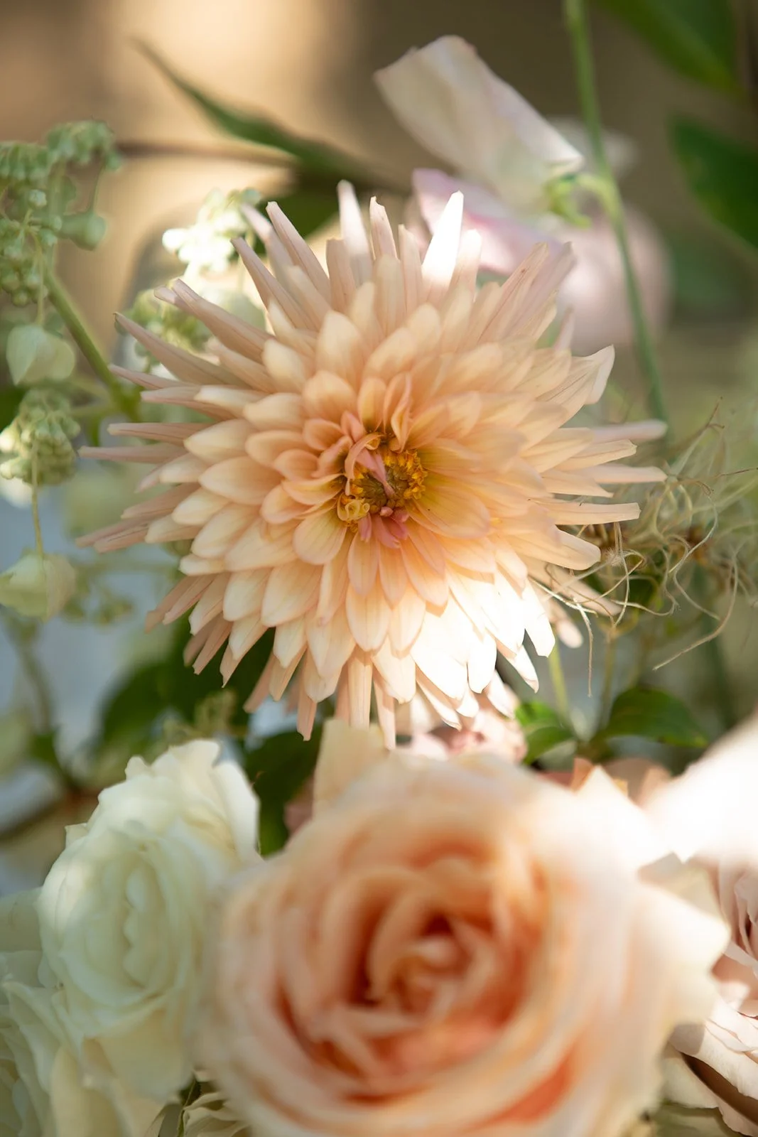 Close up of a soft paech dahlia with delicate layered petals, surrounded by seasonal foliage in a late summer wedding table arrangement.