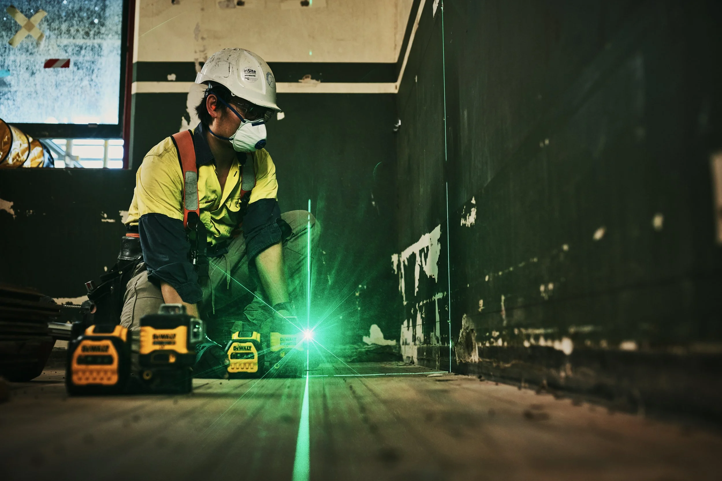 Construction worker wearing a helmet and safety mask working on a wall with a green laser level projection.